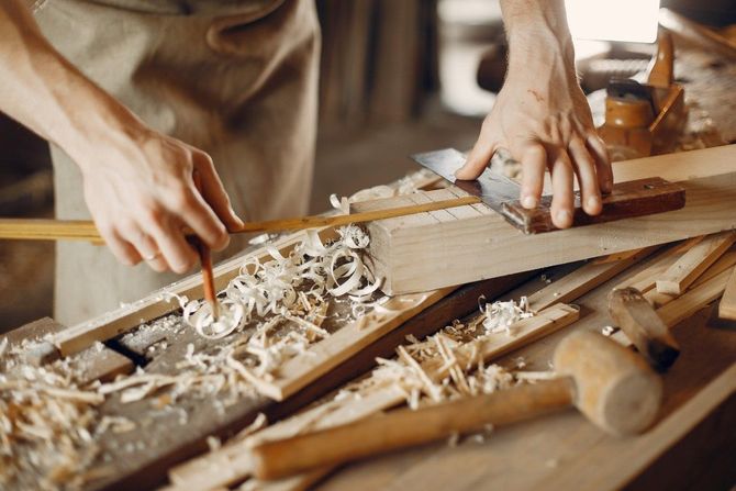 Hands planing wood on a workbench, with shavings scattered around woodworking tools.