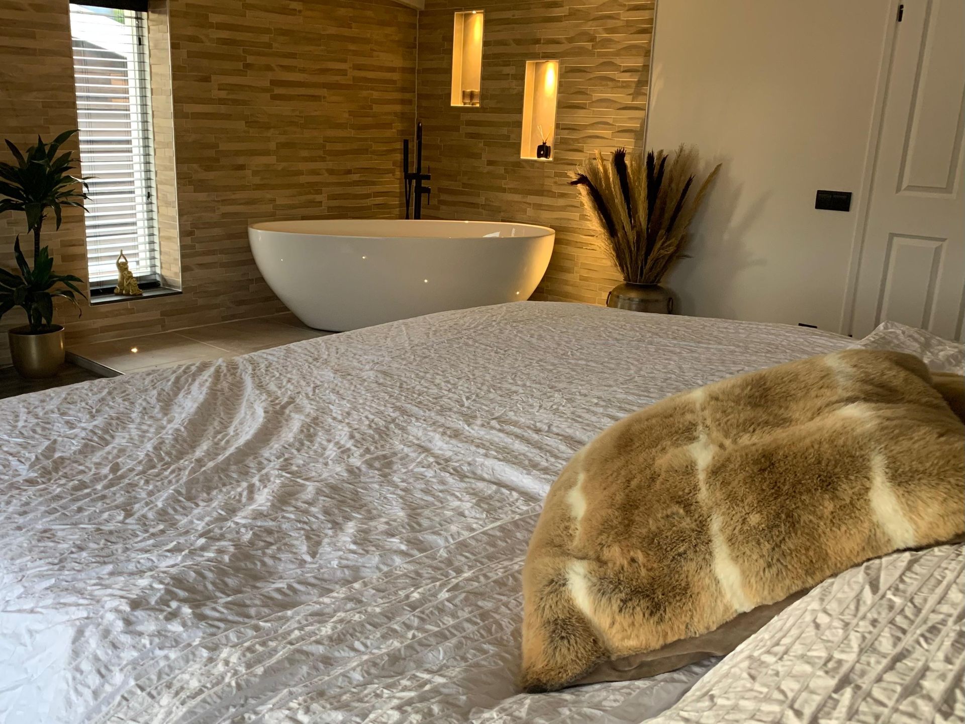 Gezellige slaapkamer met stenen muur, vrijstaand bad en bed met wit beddengoed en beige plaid.