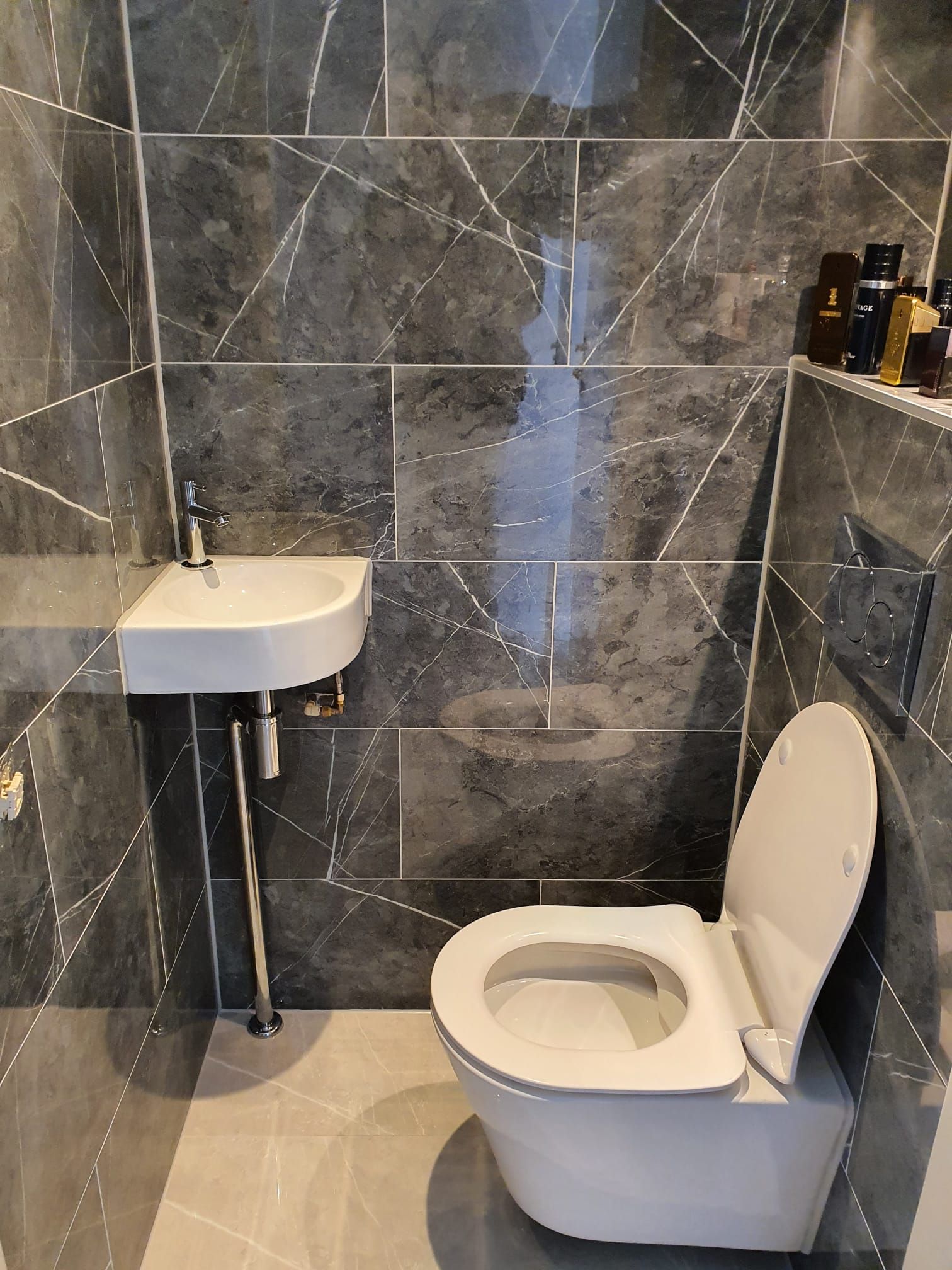 Kleine betegelde badkamer met aan de muur gemonteerde wastafel, toilet en toiletrolhouder.