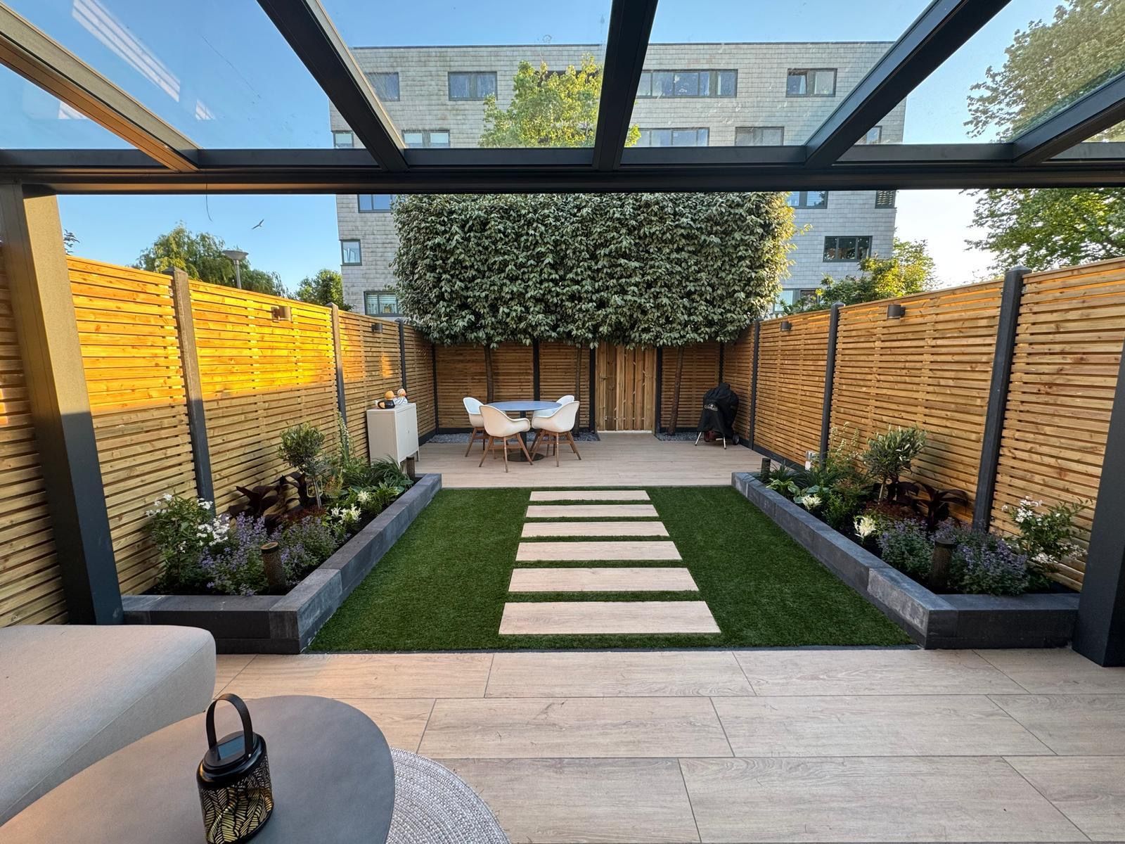 Moderne achtertuin met pergola, verhoogde plantenbakken, stapstenen en een kleine zithoek te midden van groen.