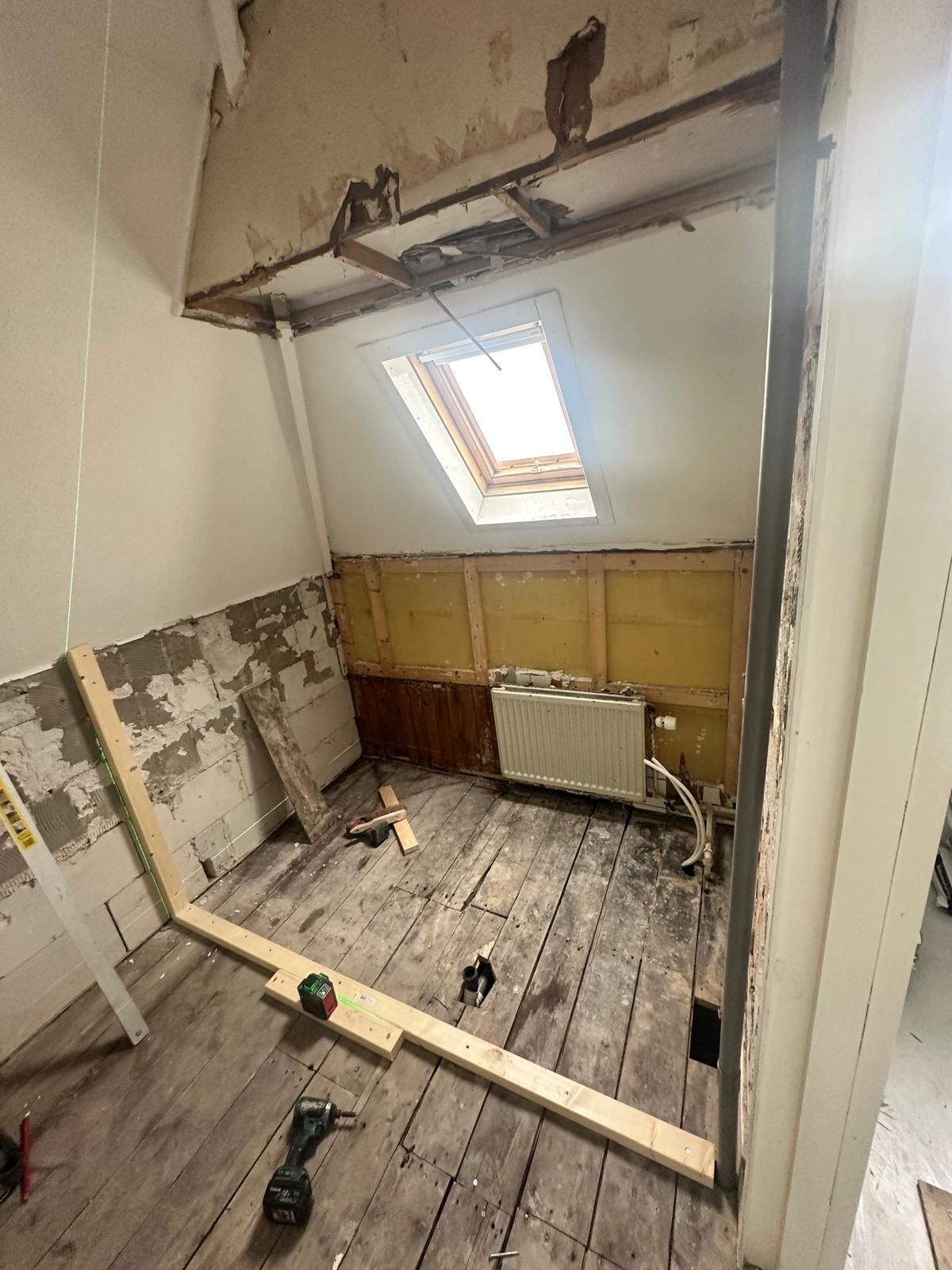 Beschadigde zolderkamer in renovatie met zichtbaar plafond, dakraam, beschadigde vloer en bouwmaterialen.