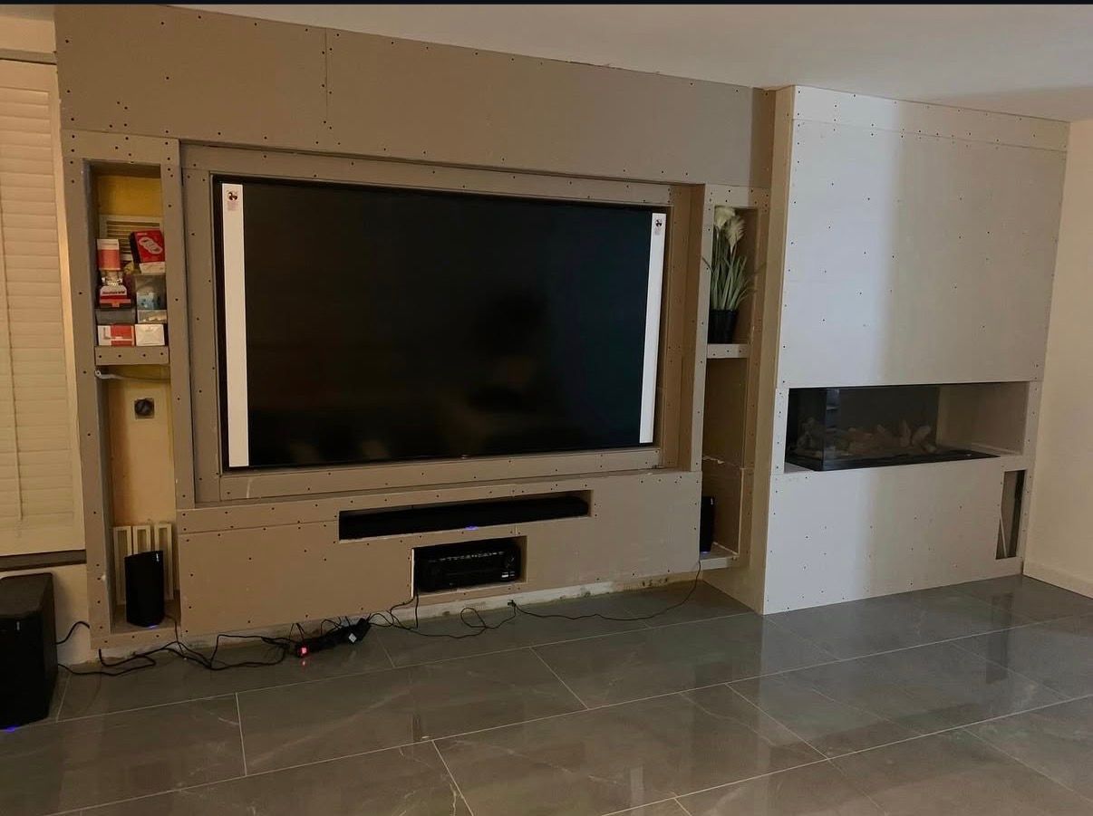 Woonkamer met een grote aan de muur gemonteerde tv en ingebouwde planken, in neutrale beigetinten.
