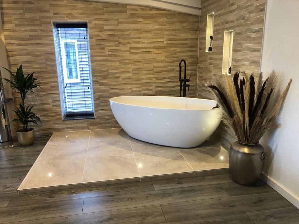 Moderne badkamer met een vrijstaand wit bad, stenen tegels op de muren en een plant bij de deur.