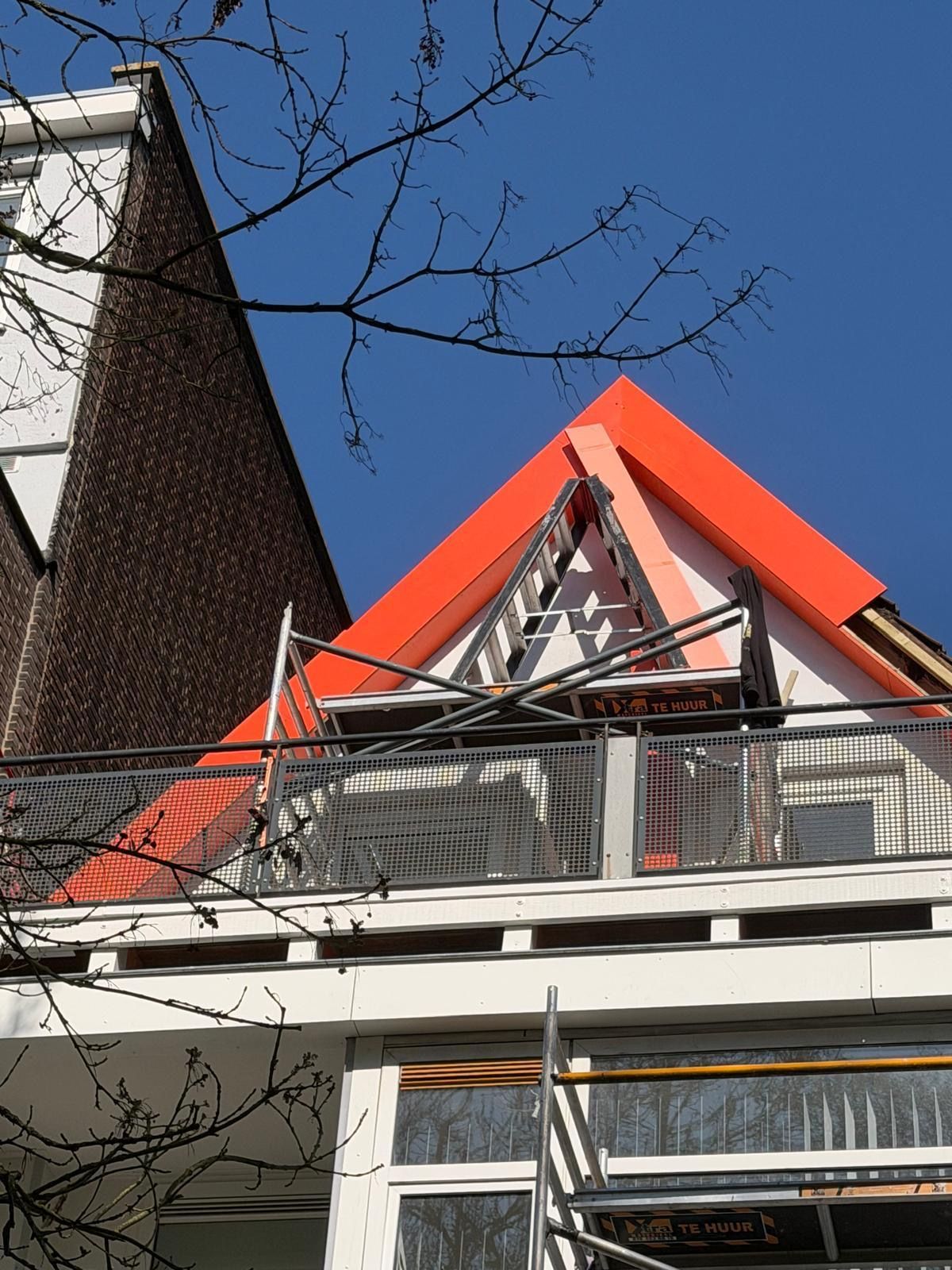 Gebouw met rood dak en balkon tegen een blauwe lucht.