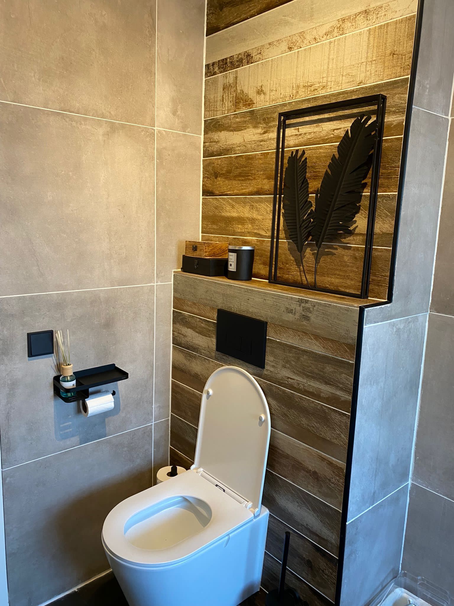 Moderne badkamer met een wit toilet, grijze tegelwanden en wanddecoratie met houten accenten.