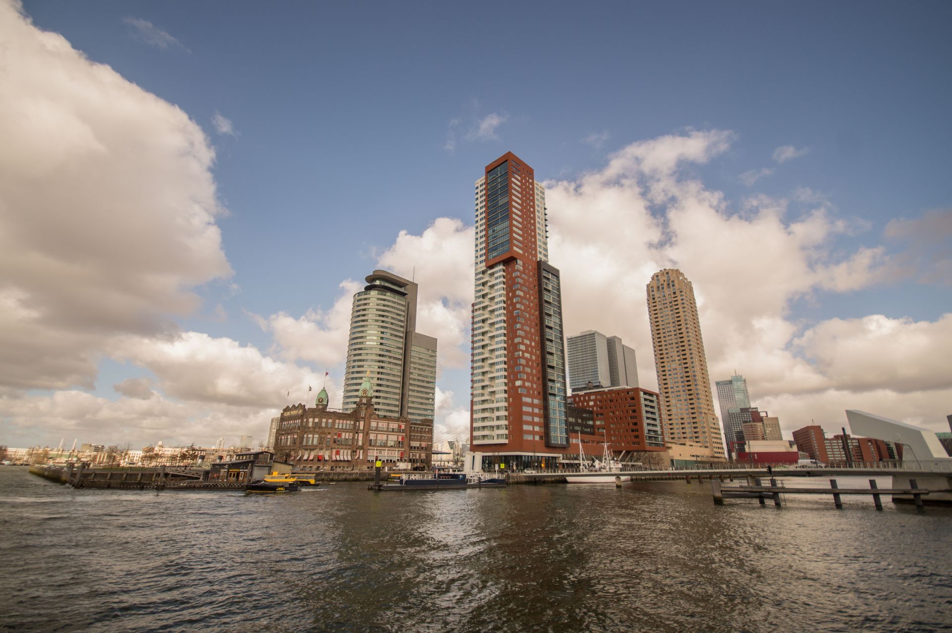 Moderne skyline aan het water met hoge appartemententorens onder een bewolkte hemel, weerspiegeld in het kalme water.