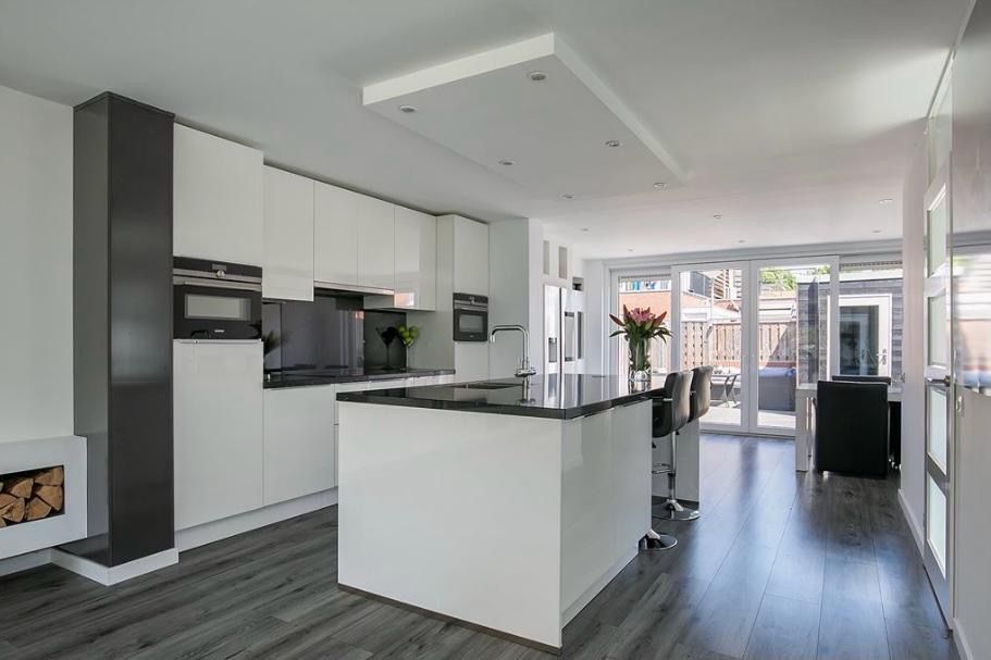 Moderne open keuken en woonkamer met witte kasten, donkere vloer en grote glazen deuren naar het terras.