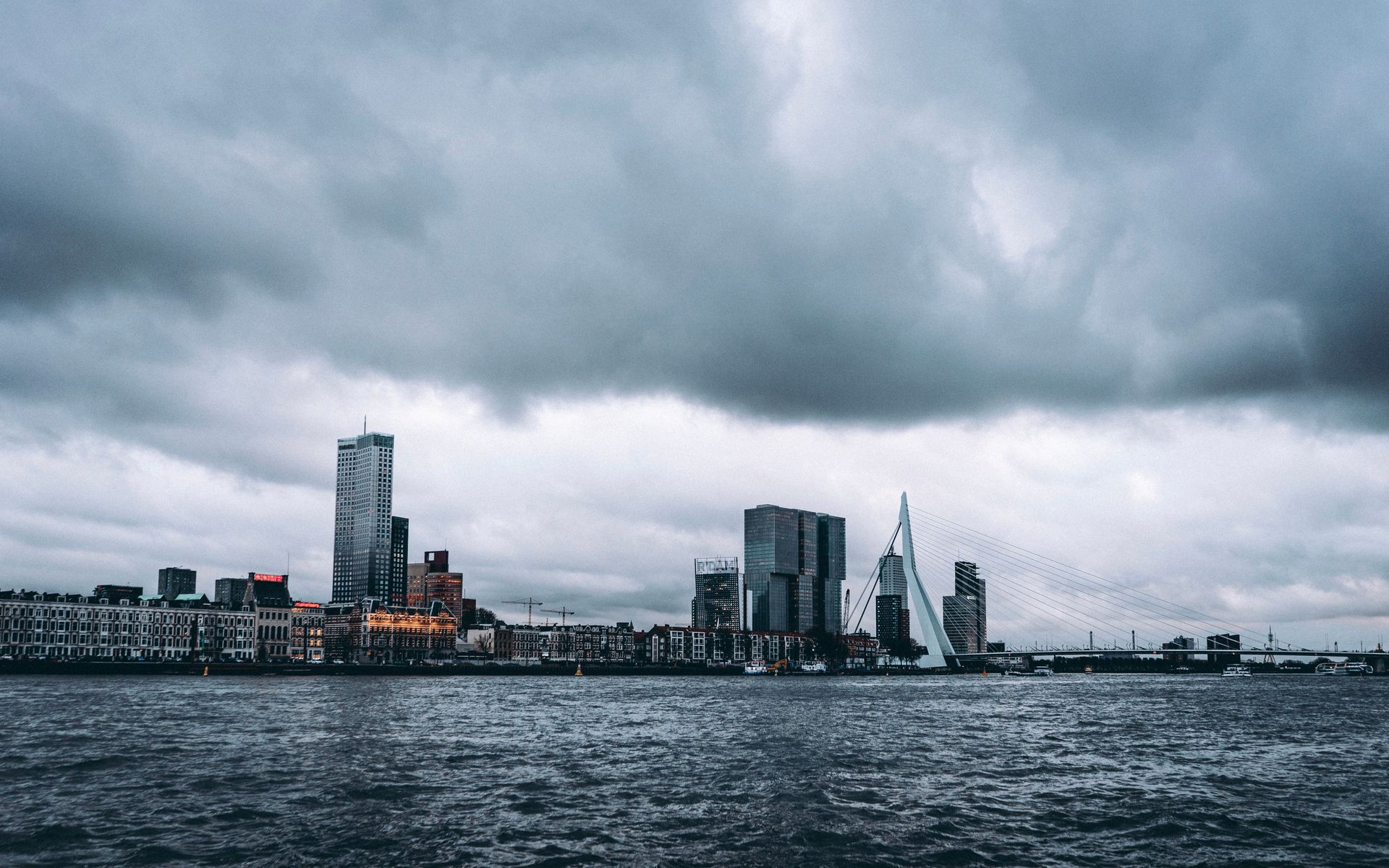 Stadsgezicht met hoge, moderne gebouwen onder donkere stormwolken boven een woelige waterkant