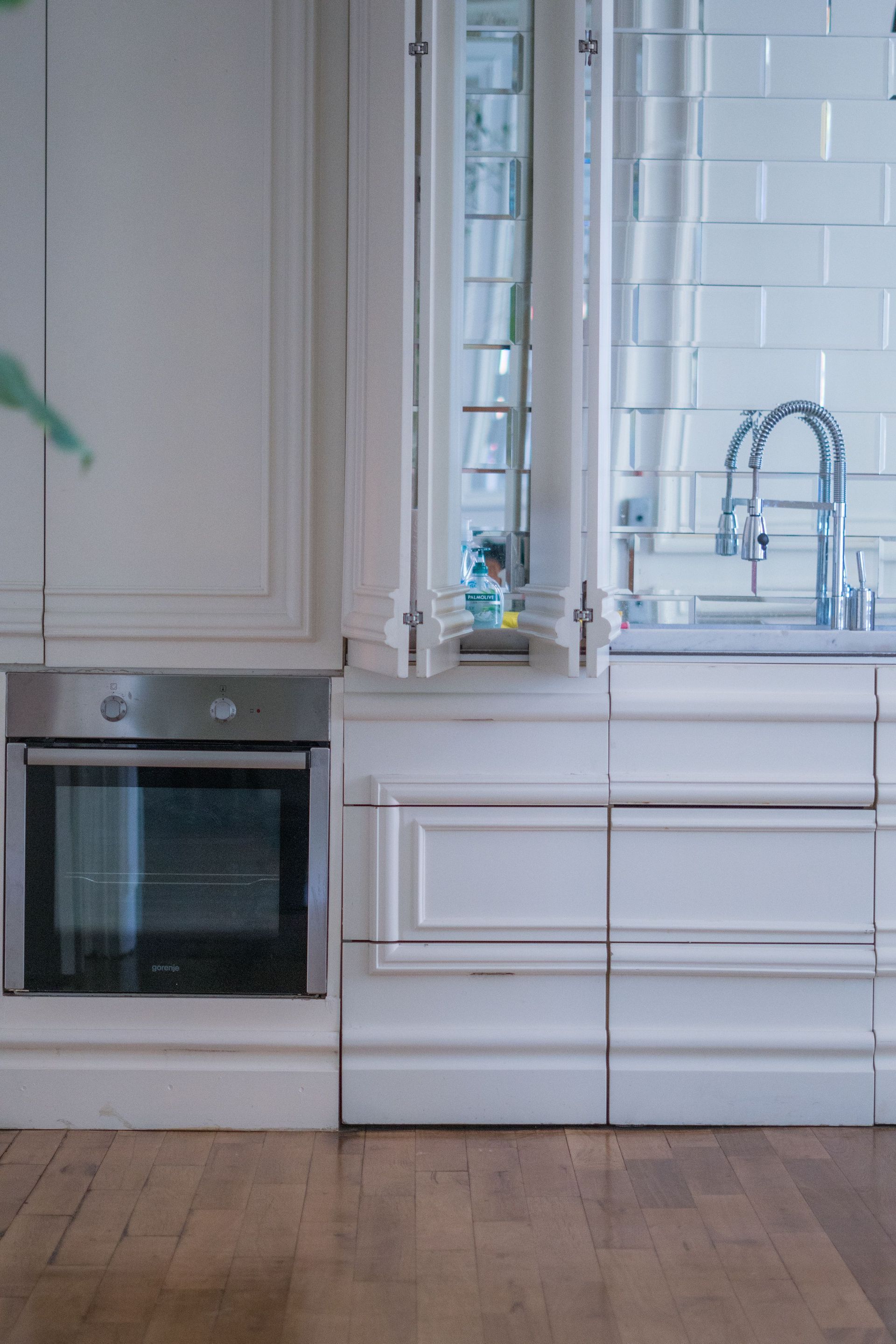 Moderne witte keuken met ingebouwde oven, raam en chromen kraan boven de spoelbak.
