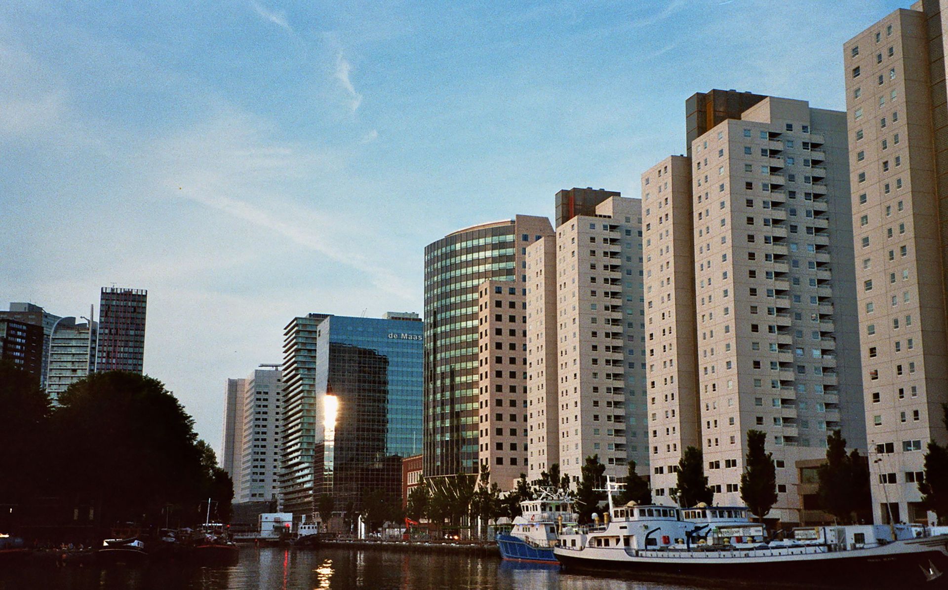 De skyline langs het water met hoge appartementencomplexen onder een helderblauwe hemel, weerspiegeld in het kalme water.