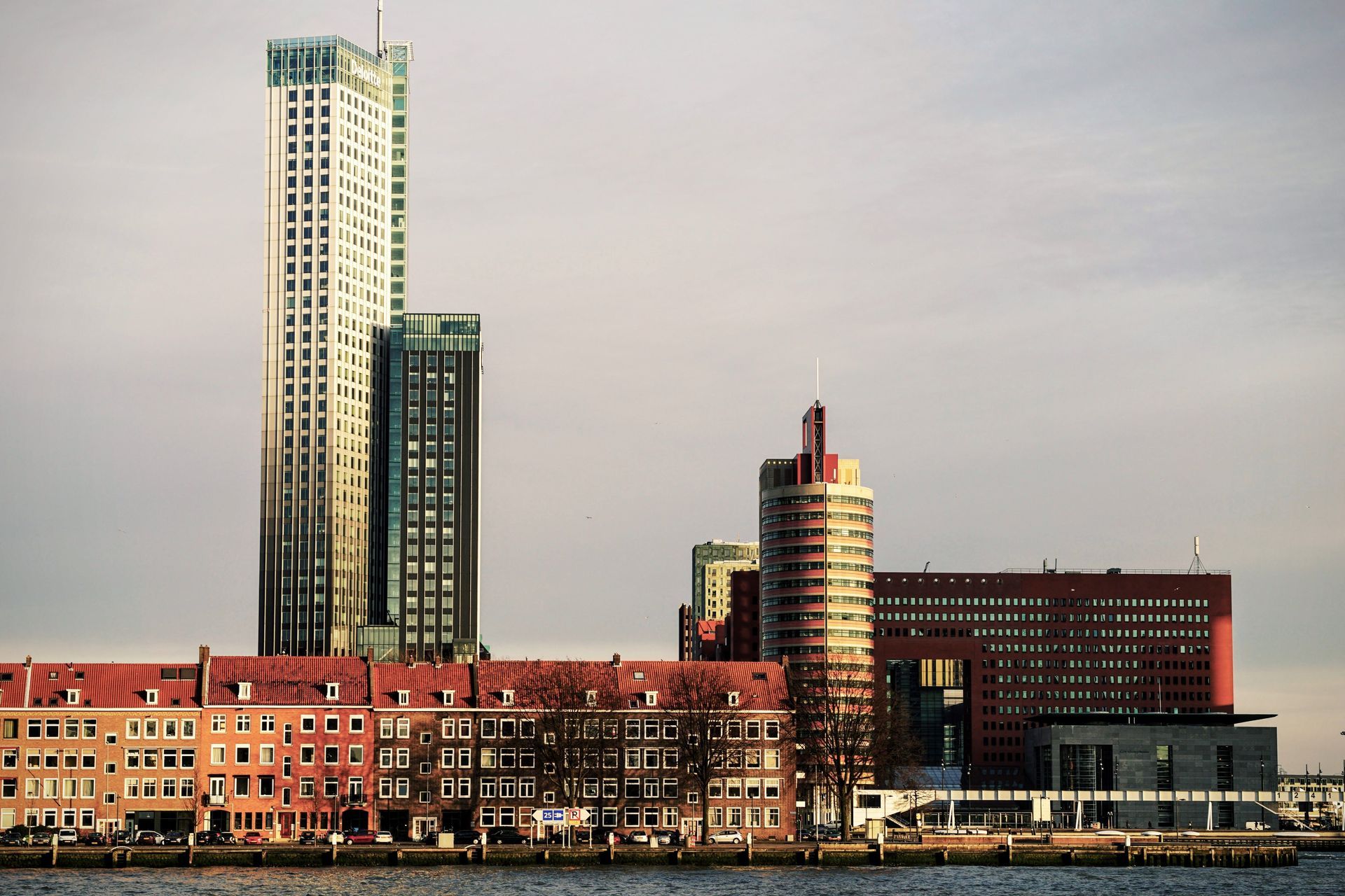 De skyline van de waterkant met hoge, moderne torens en gebouwen van rode baksteen onder een bewolkte hemel.