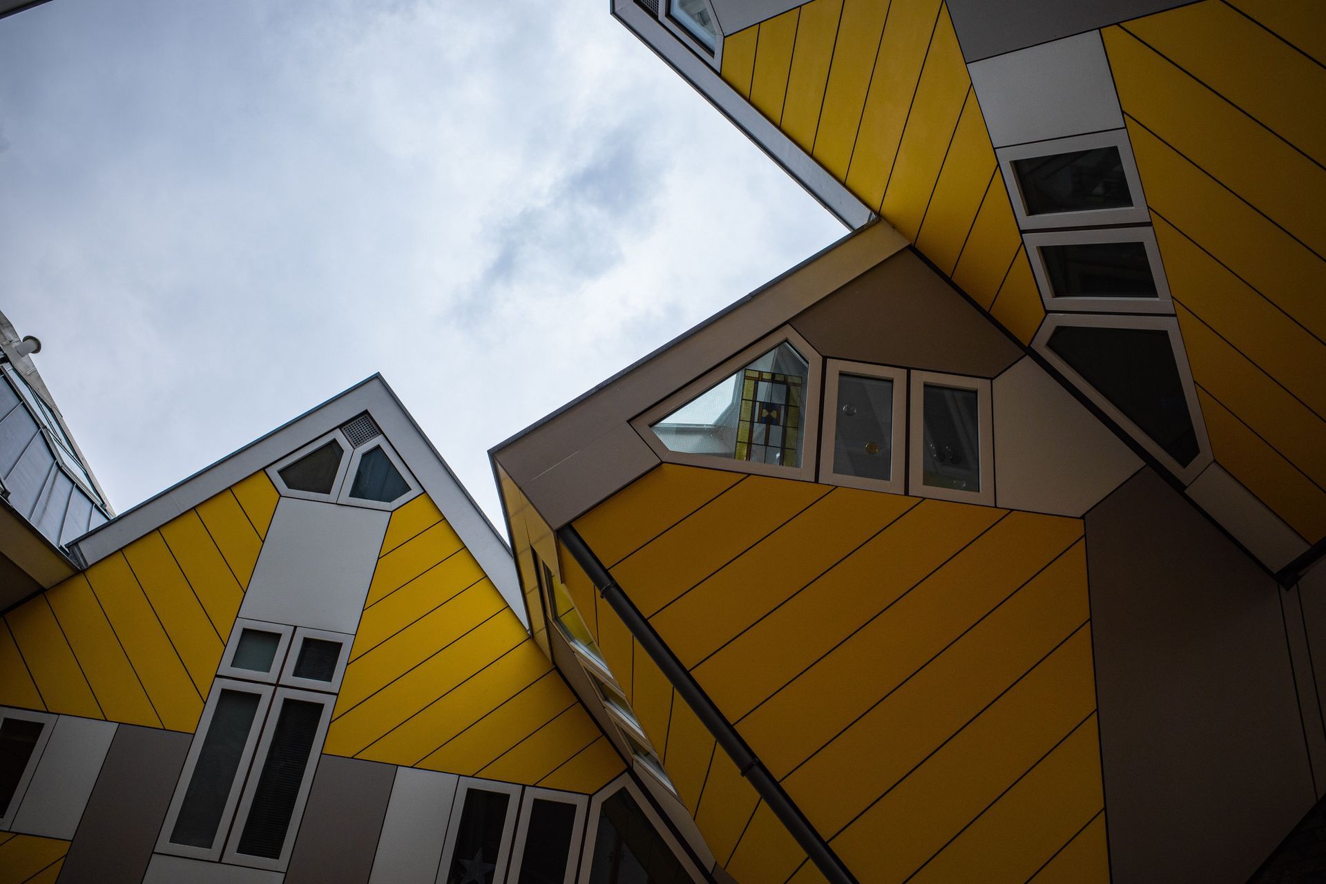 Moderne, hoekige huizen met gele panelen, van onderaf gezien tegen een bewolkte hemel.