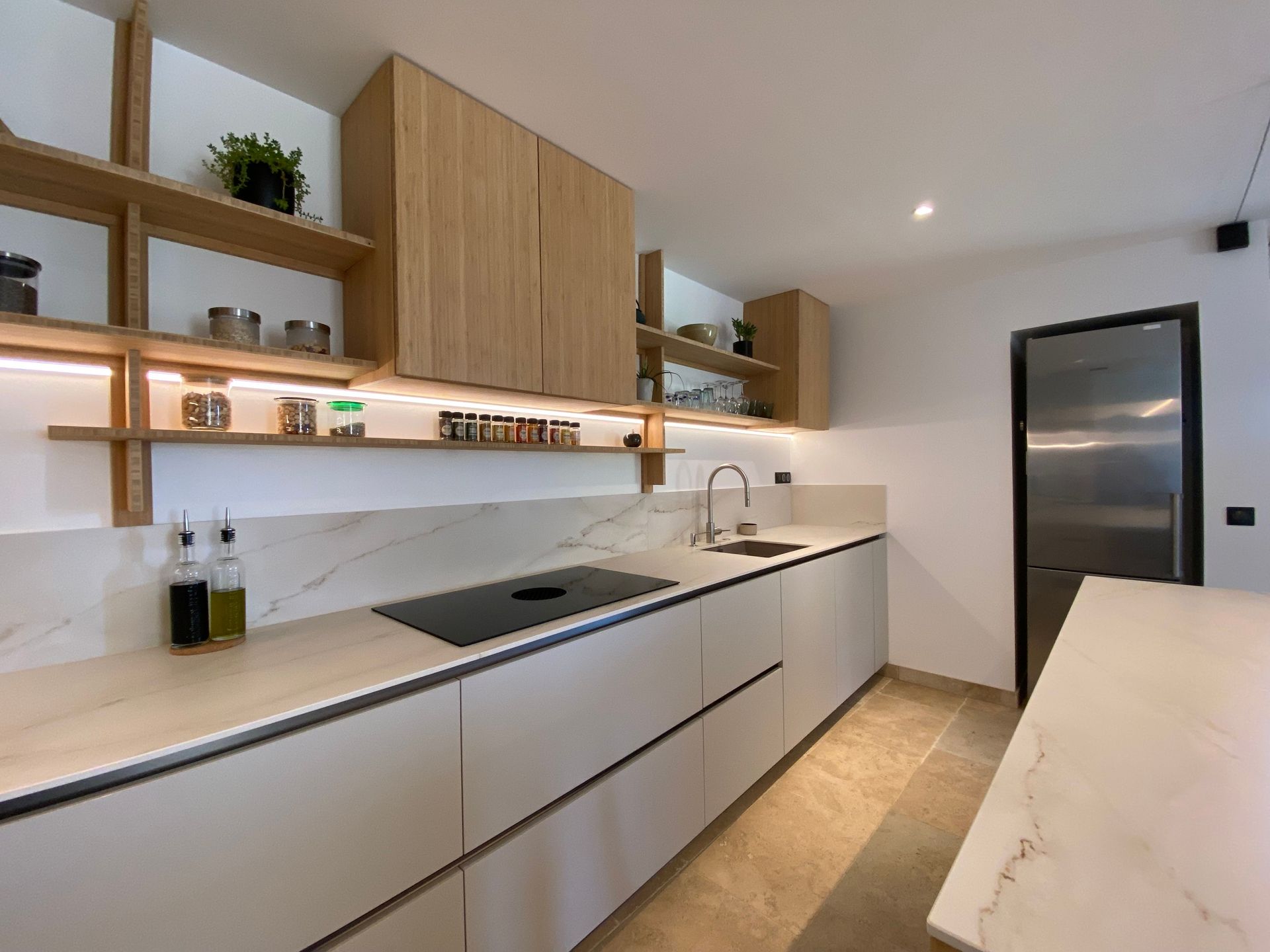 Moderne minimalistische keuken met witte kasten, houten accenten, marmeren kookeiland en ingebouwde planken.