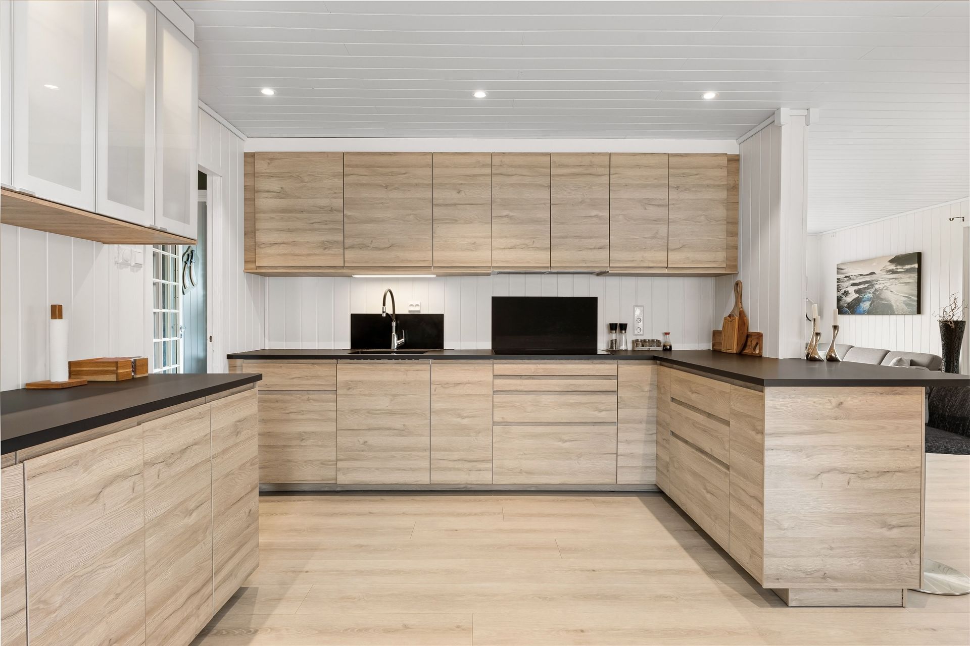 Moderne minimalistische keuken met lichte houten kasten, zwarte werkbladen en witte muren.