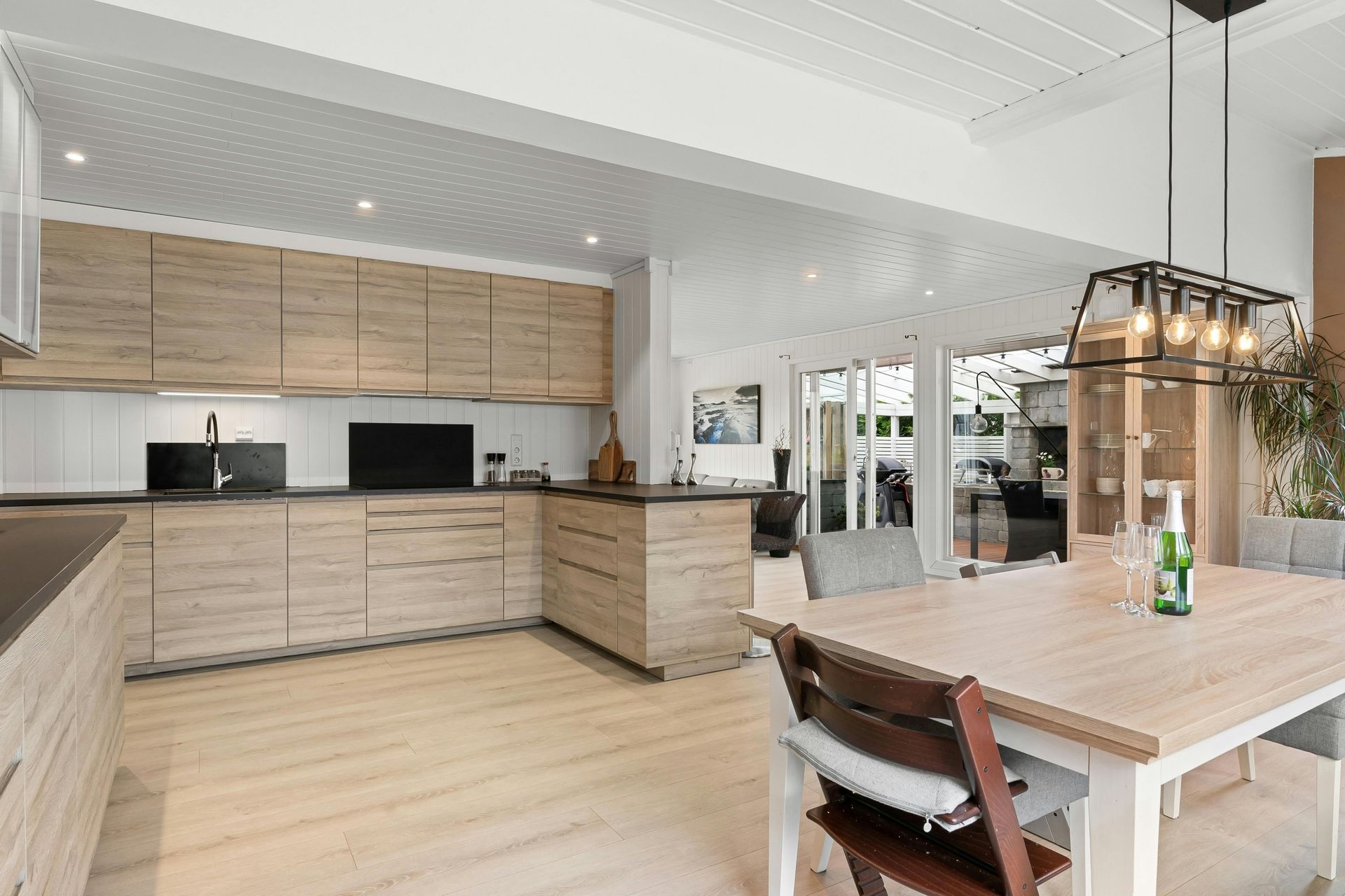 Lichte, moderne keuken en eethoek met lichte houten kasten, witte muren en een houten tafel.
