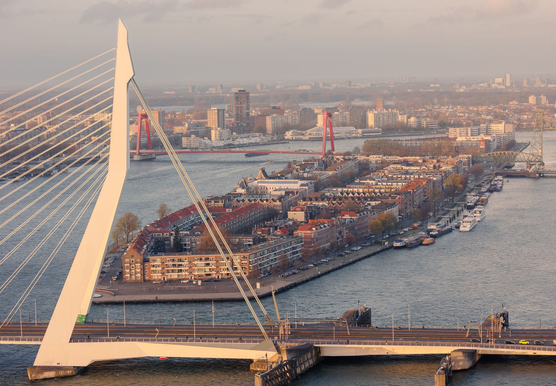 Luchtfoto van een kabelbrug over een rivier met een drukke haven en stadsgezicht op de achtergrond.