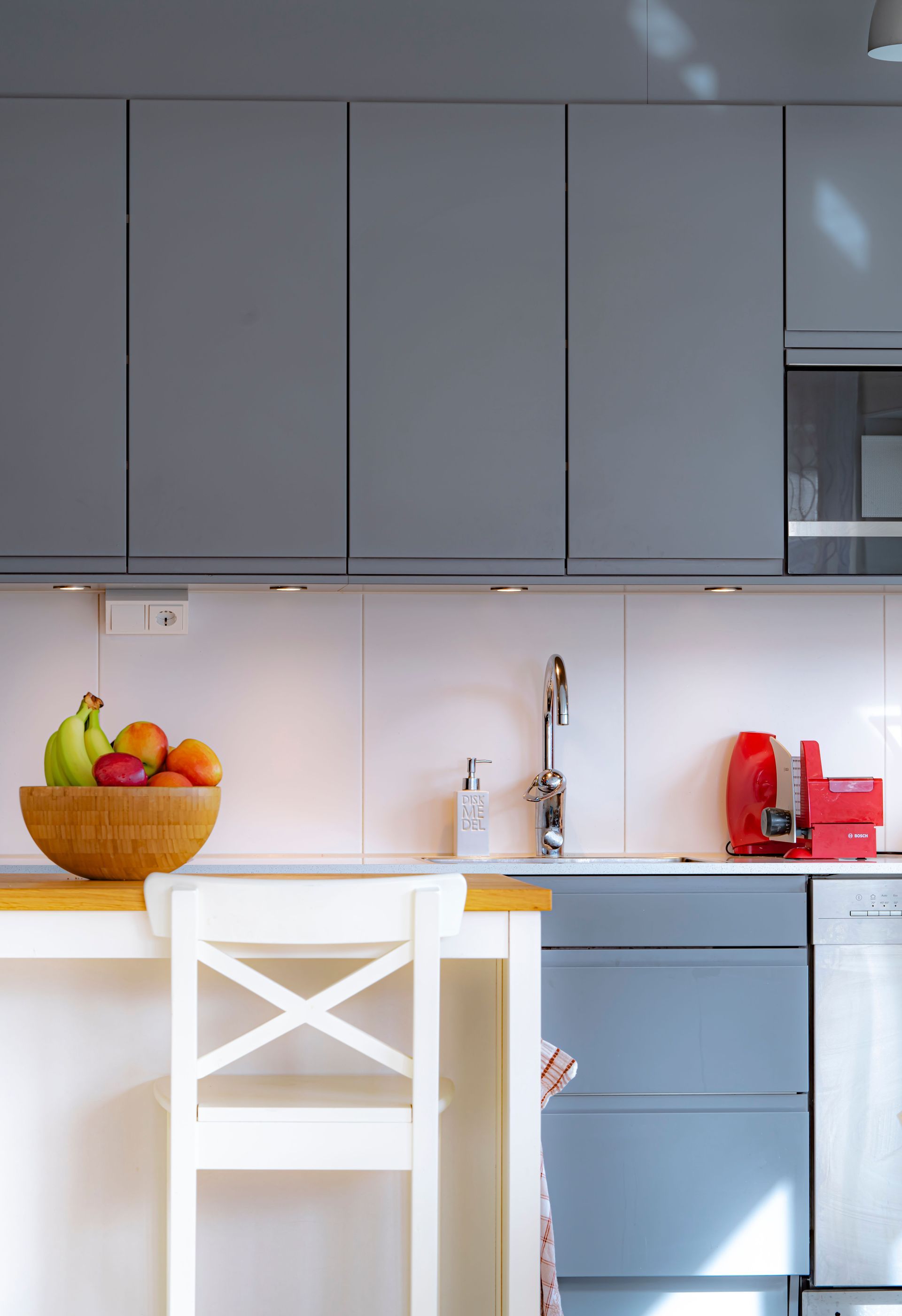 Moderne keuken met grijze kasten, wit kookeiland, fruitschaal en rode apparaten.