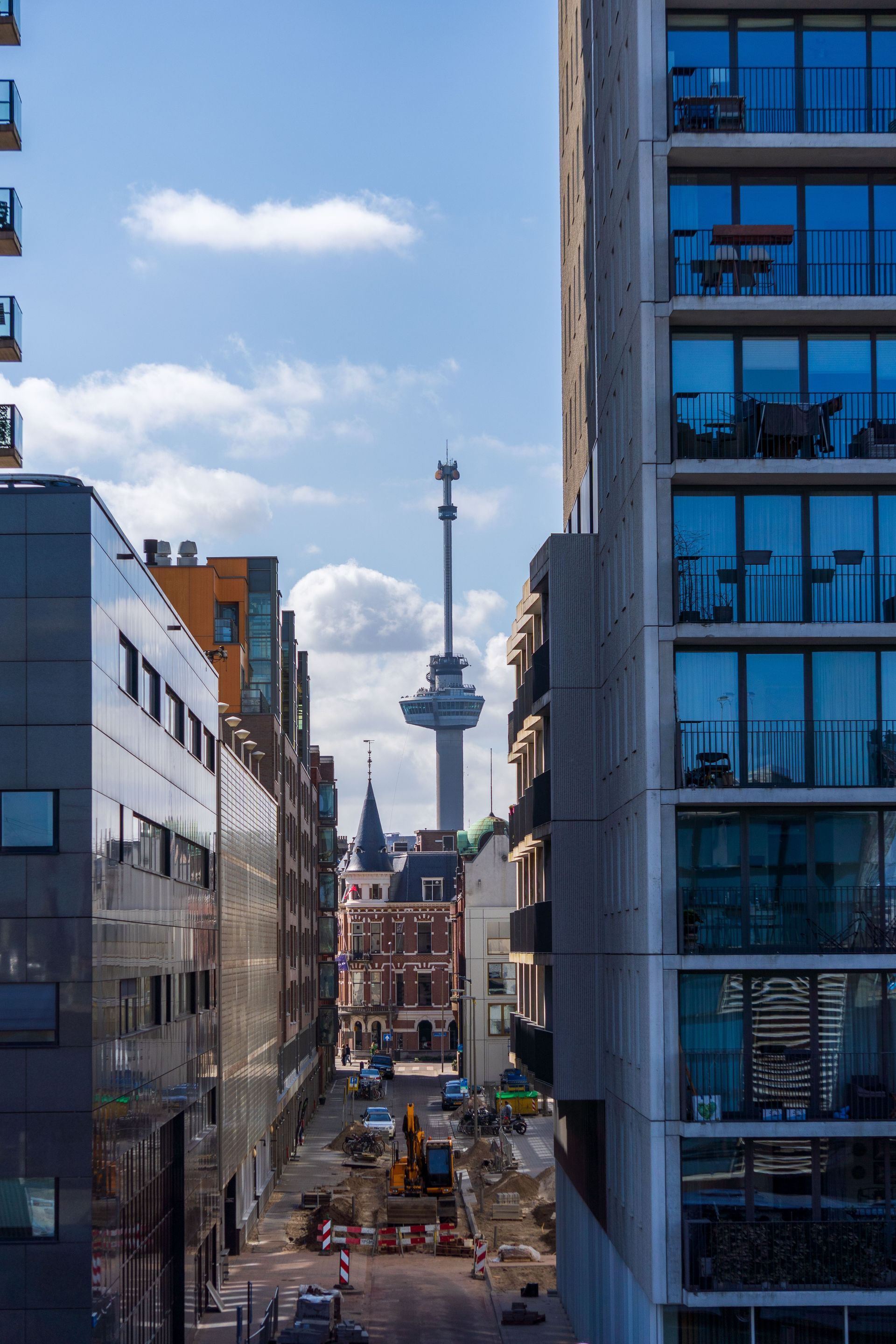 Stadsgezicht met moderne gebouwen op de achtergrond, en een toren in de verte tegen een blauwe hemel.