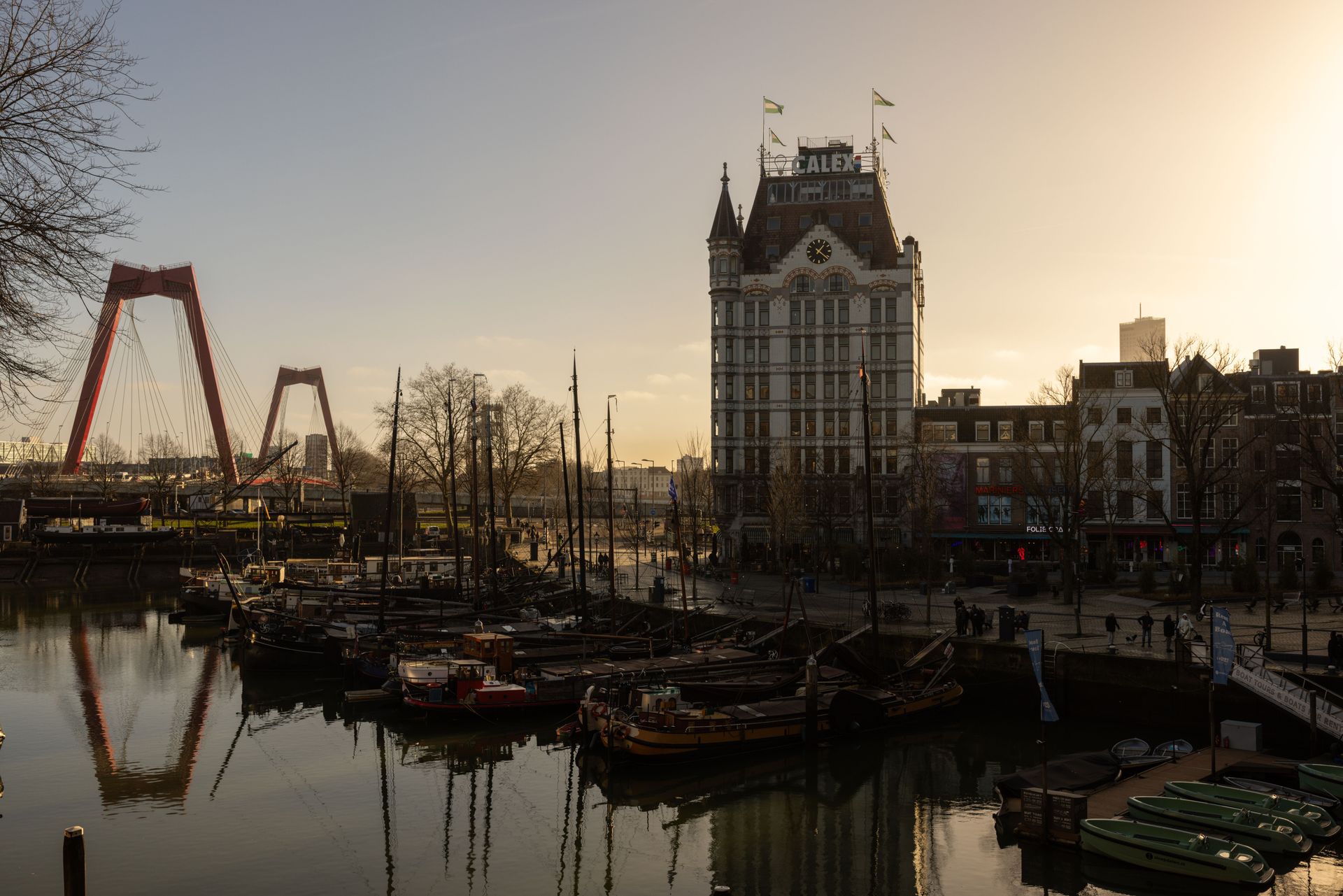 De haven bij zonsondergang met boten, een hoog historisch gebouw en een rode kraanvogel die weerspiegeld wordt in het water.