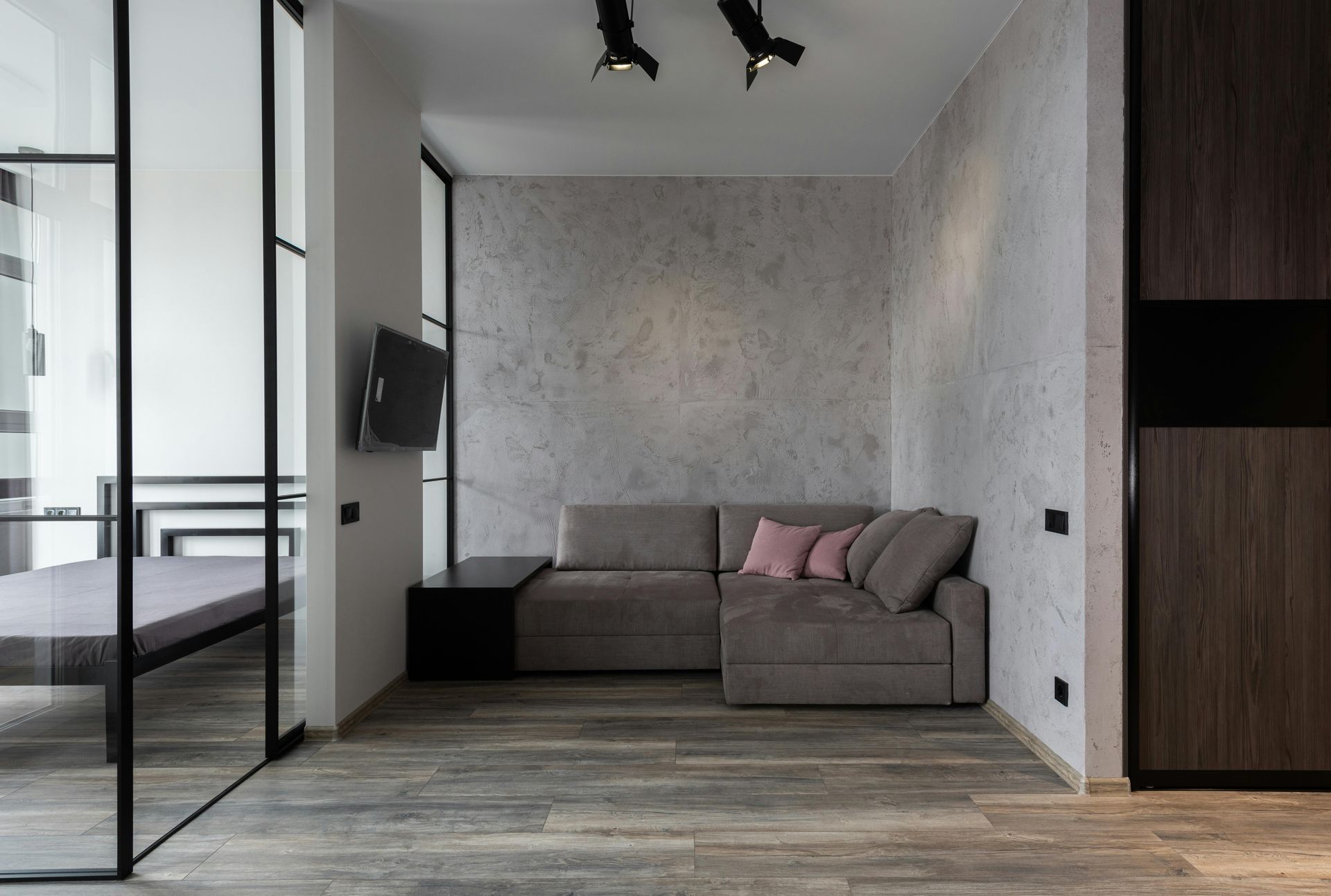 Moderne, minimalistische woonkamer met grijze hoekbank, aan de muur gemonteerde tv en houten vloer.