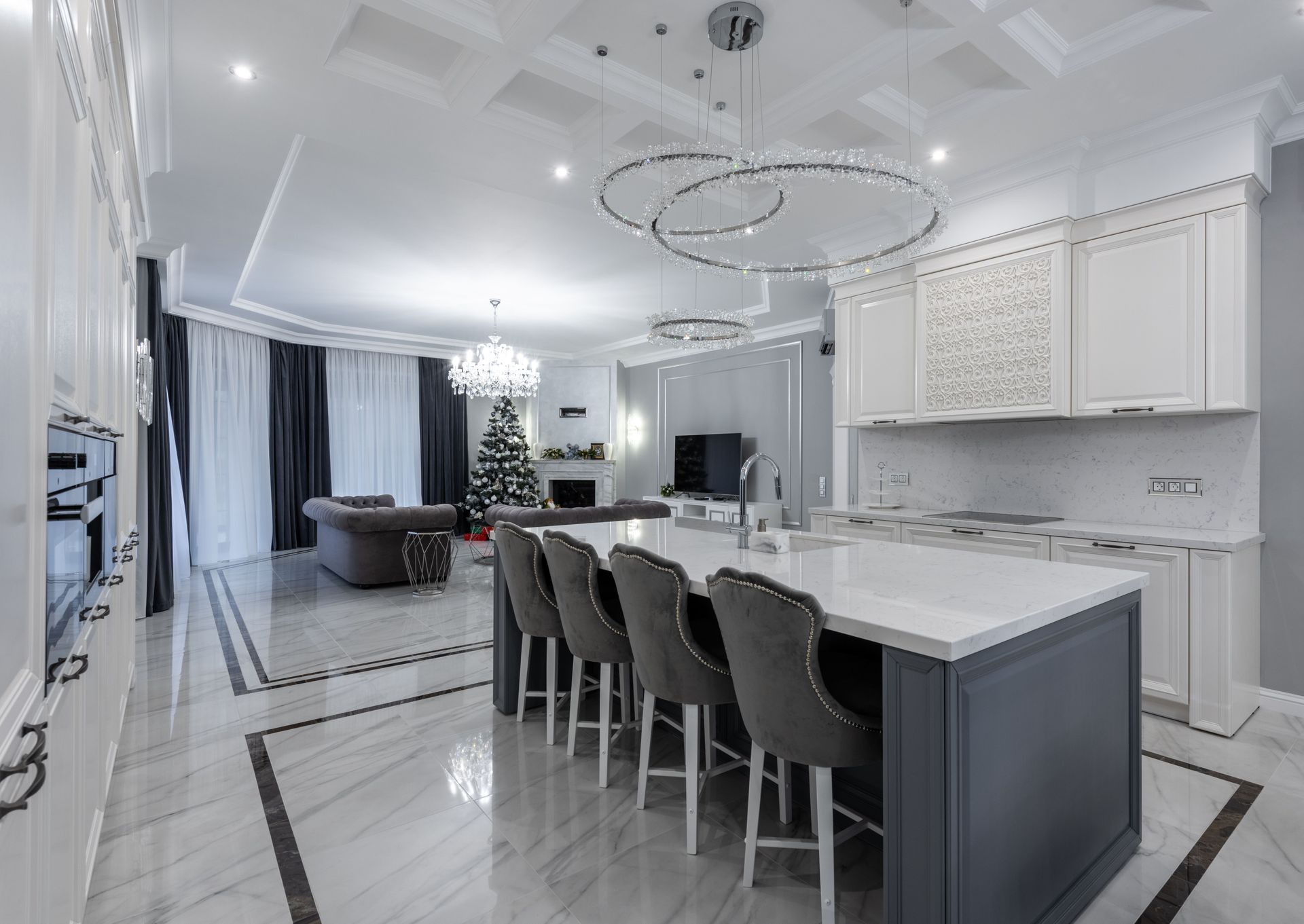 Lichte, moderne open keuken en woonkamer met witte kasten, grijze barkrukken aan het kookeiland en een kroonluchter.