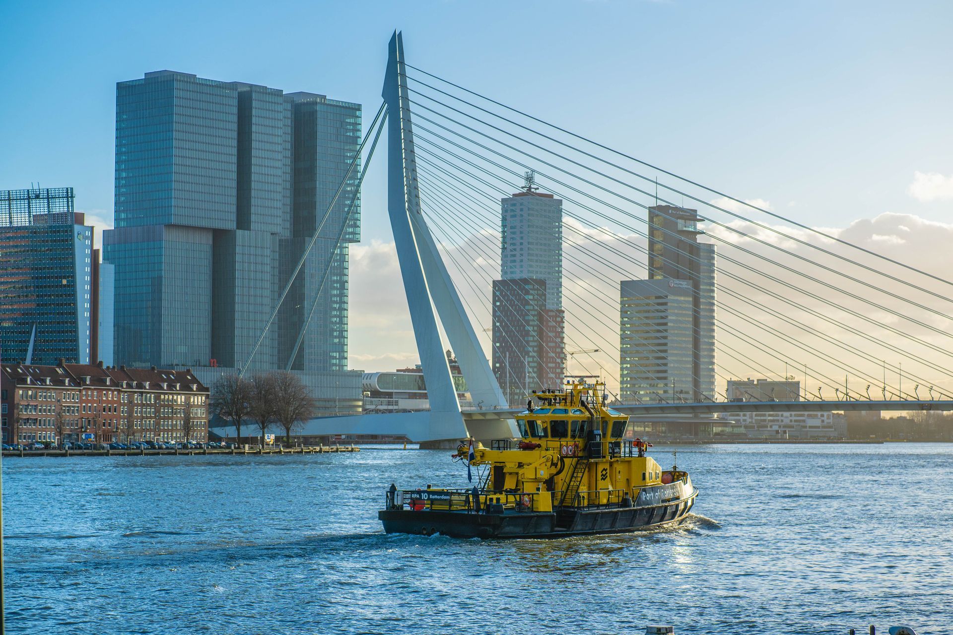 Gele sleepboot op een rivier voor een kabelbrug en de moderne skyline van de stad