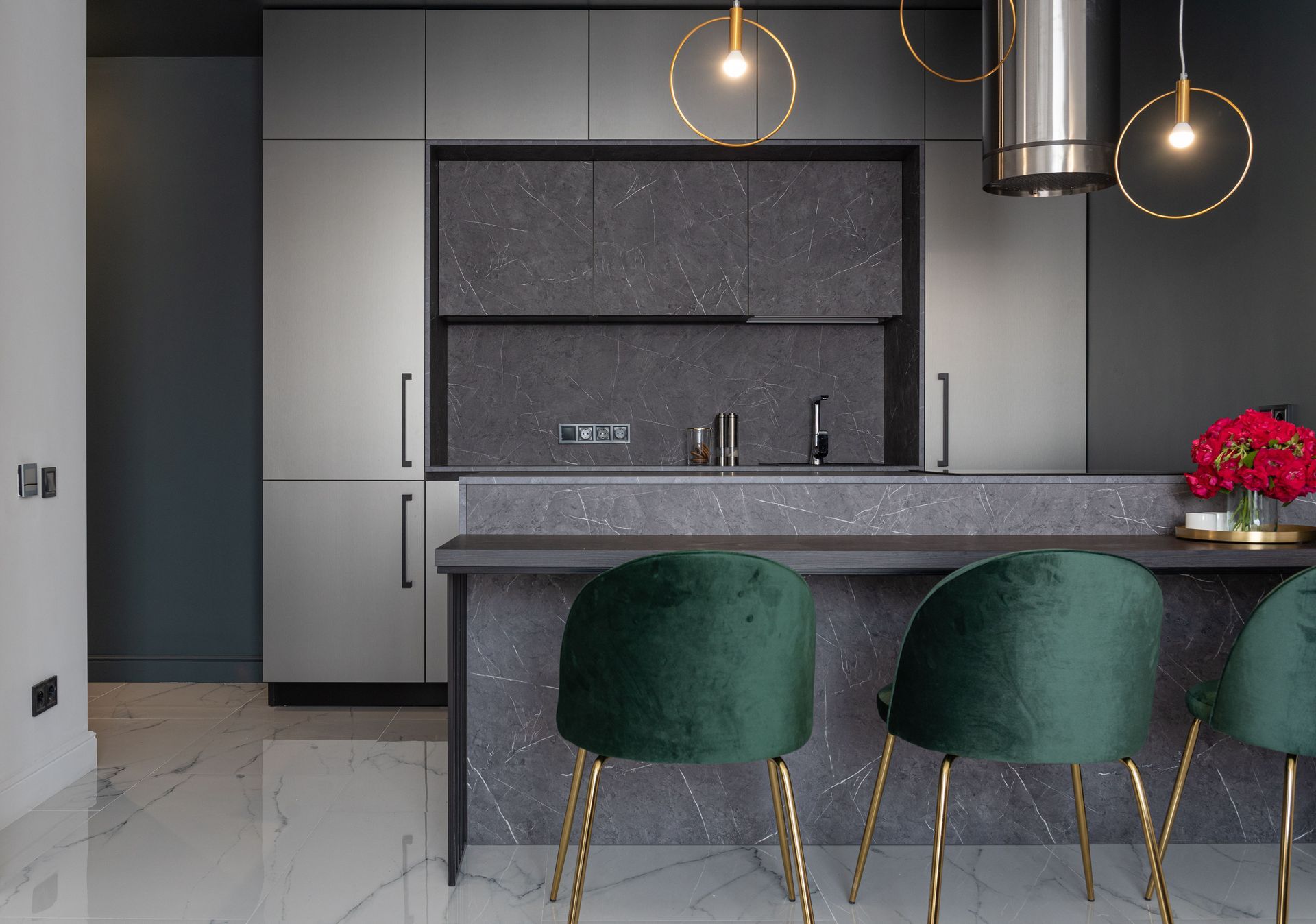 Moderne keuken met een grijs kookeiland, groene fluwelen krukken en hanglampen boven een glanzende witte vloer.