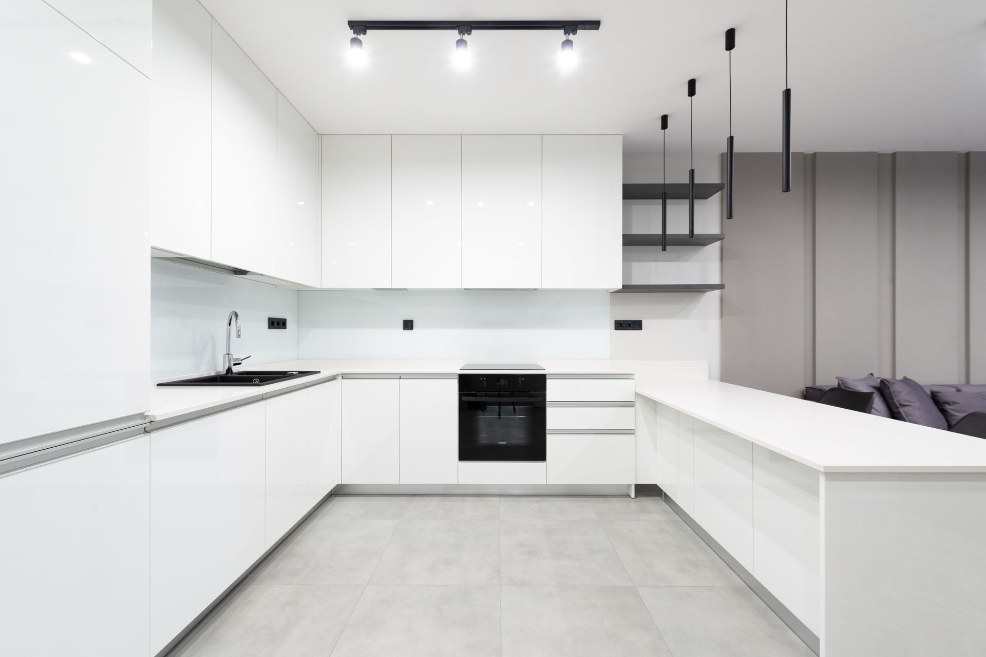 Moderne, minimalistische witte keuken met kookeiland, zwarte armaturen en grote grijze vloertegels.