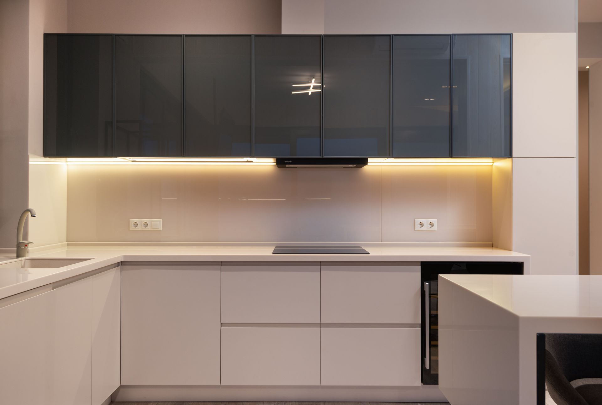 Moderne minimalistische keuken met donkere bovenkasten, witte onderkasten en warme verlichting onder de kasten.