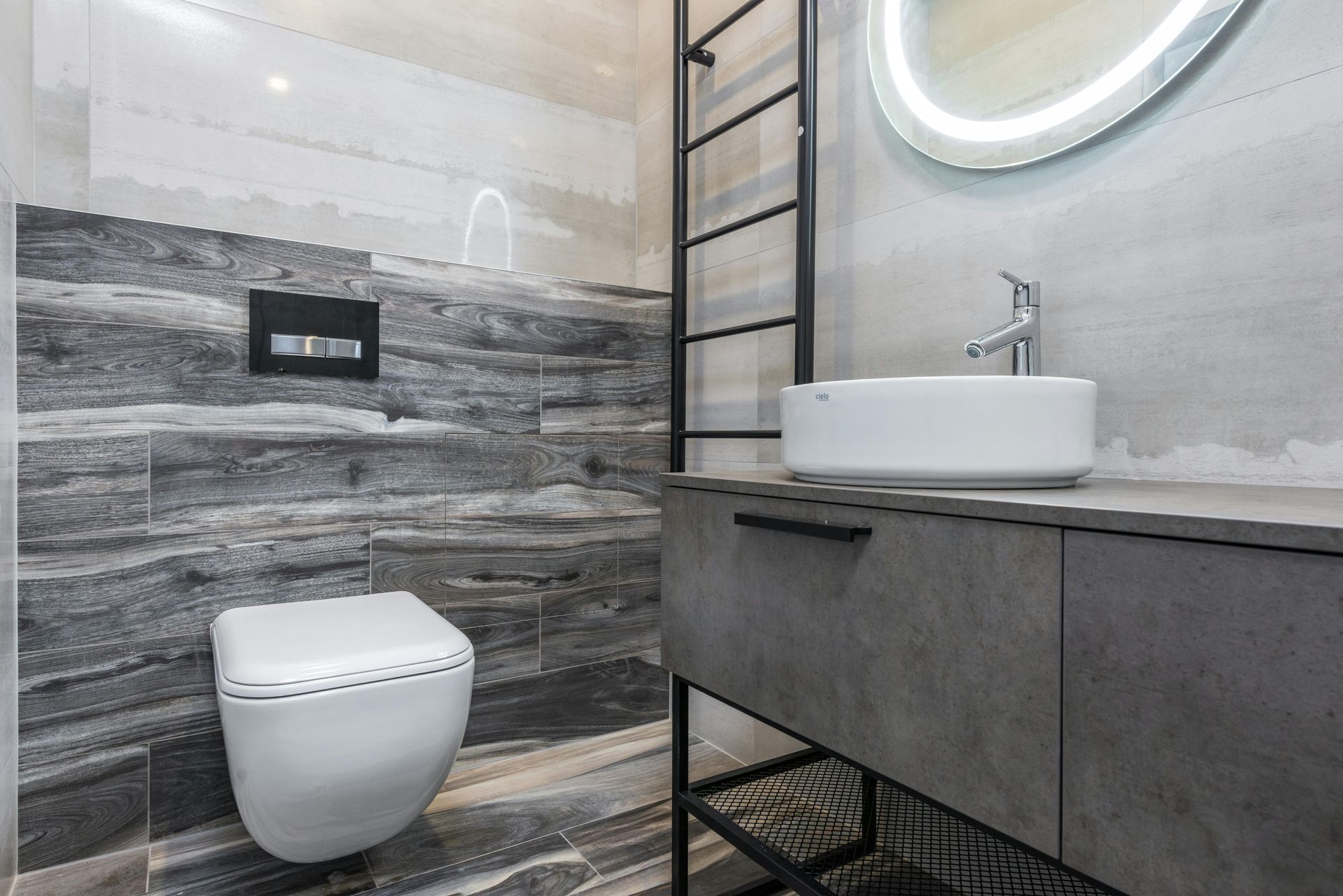 Moderne grijze badkamer met wandtoilet, wastafel, spiegel en zwarte handdoekrek.