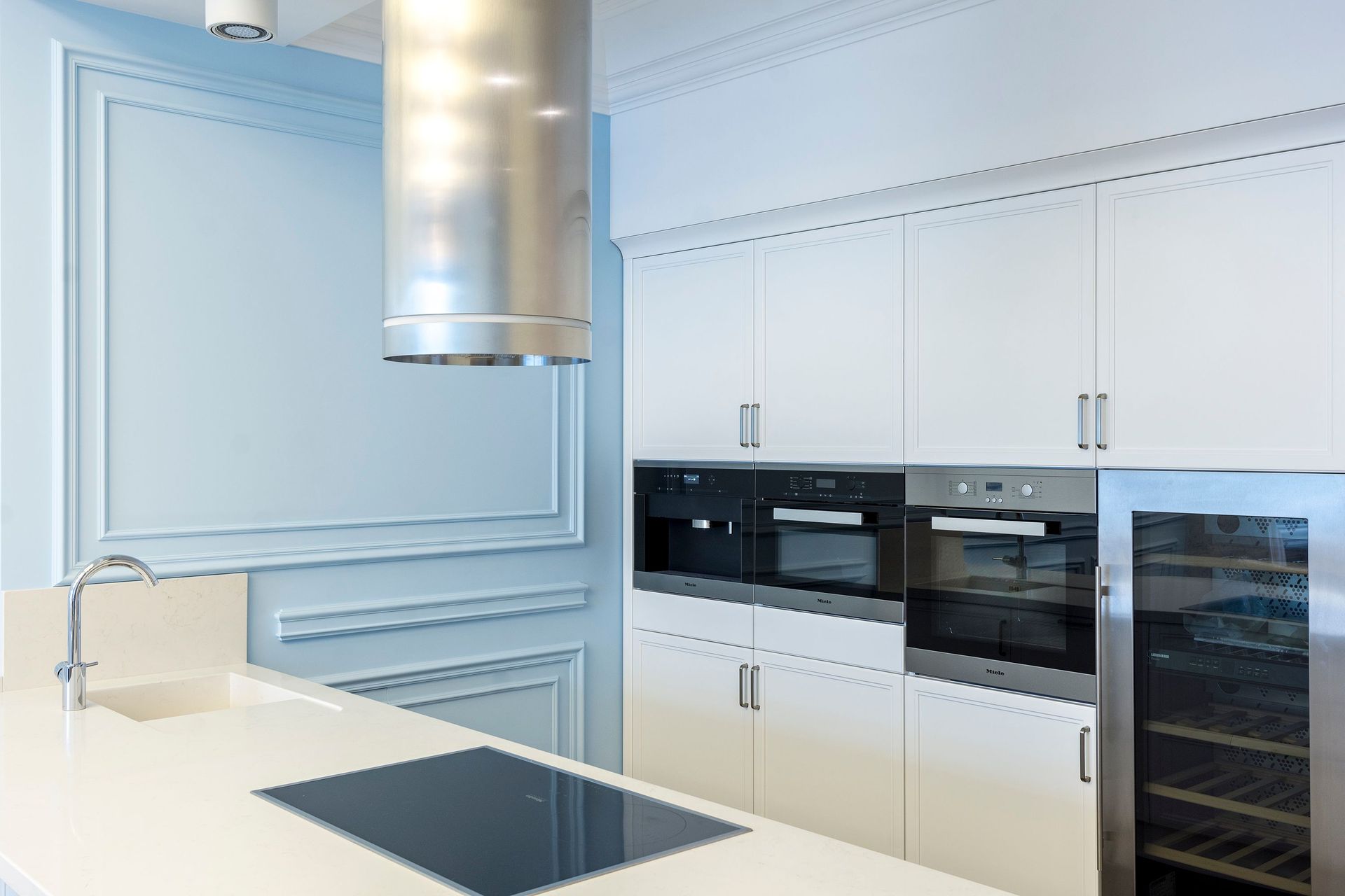 Lichte, moderne witte keuken met inbouwapparatuur, groot raam en zwart aanrechtblad met kookplaat.