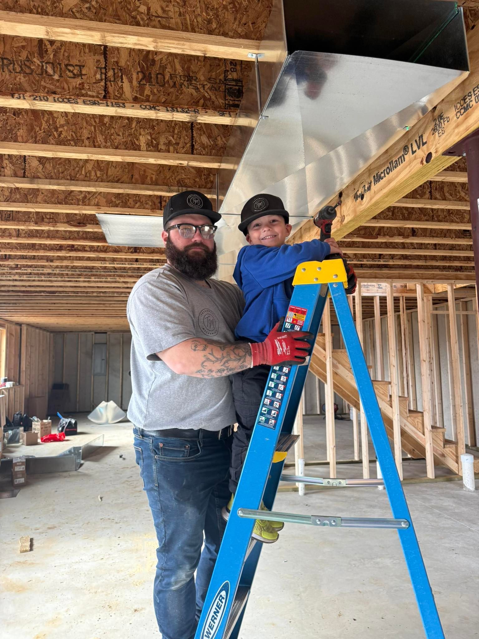 Man and child on a blue ladder installing ductwork in a building under construction.