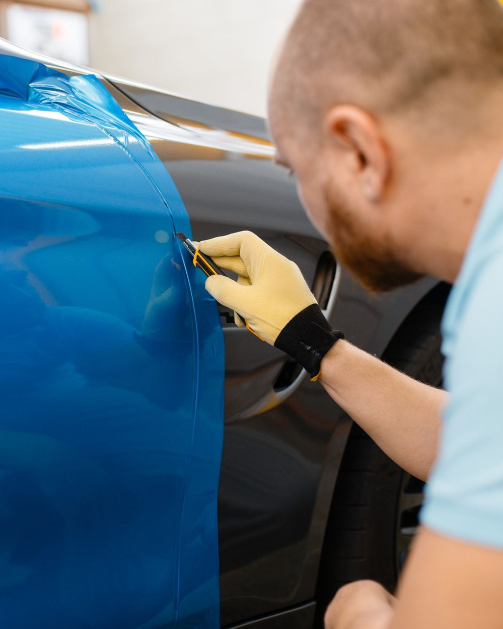 Person applying blue vinyl wrap to a car door with a tool