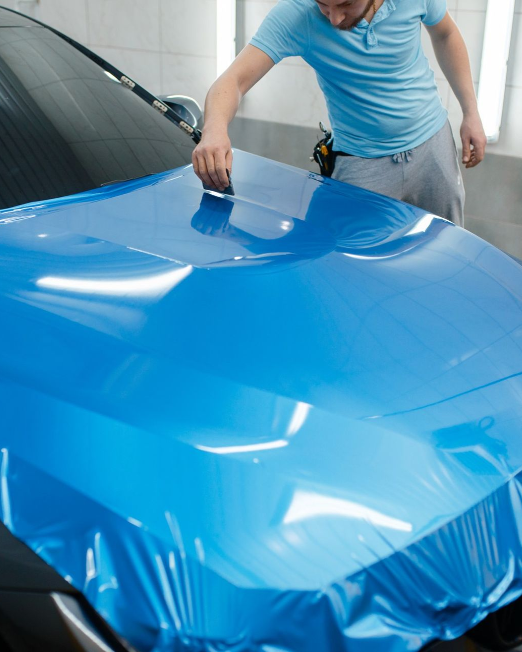 Person smoothing blue vinyl wrap over a car hood in a garage