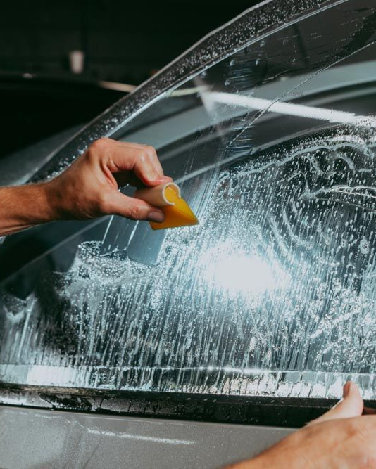 Hand scraping ice from a car window with a yellow tool on a snowy, wet windshield