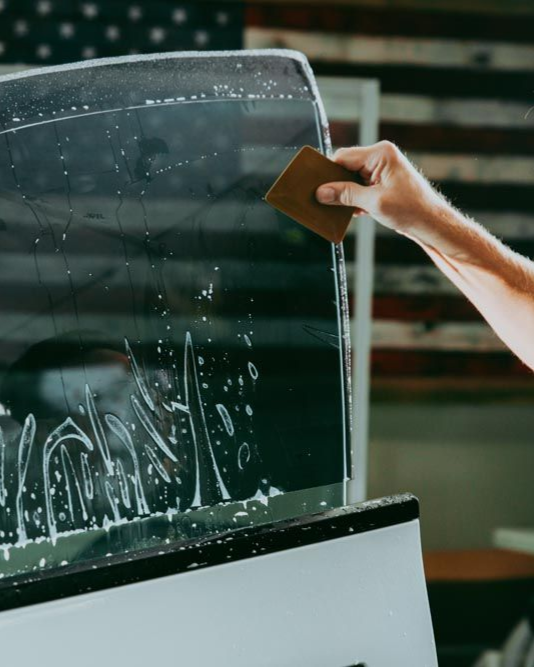 Hand wiping a wet car window with a sponge