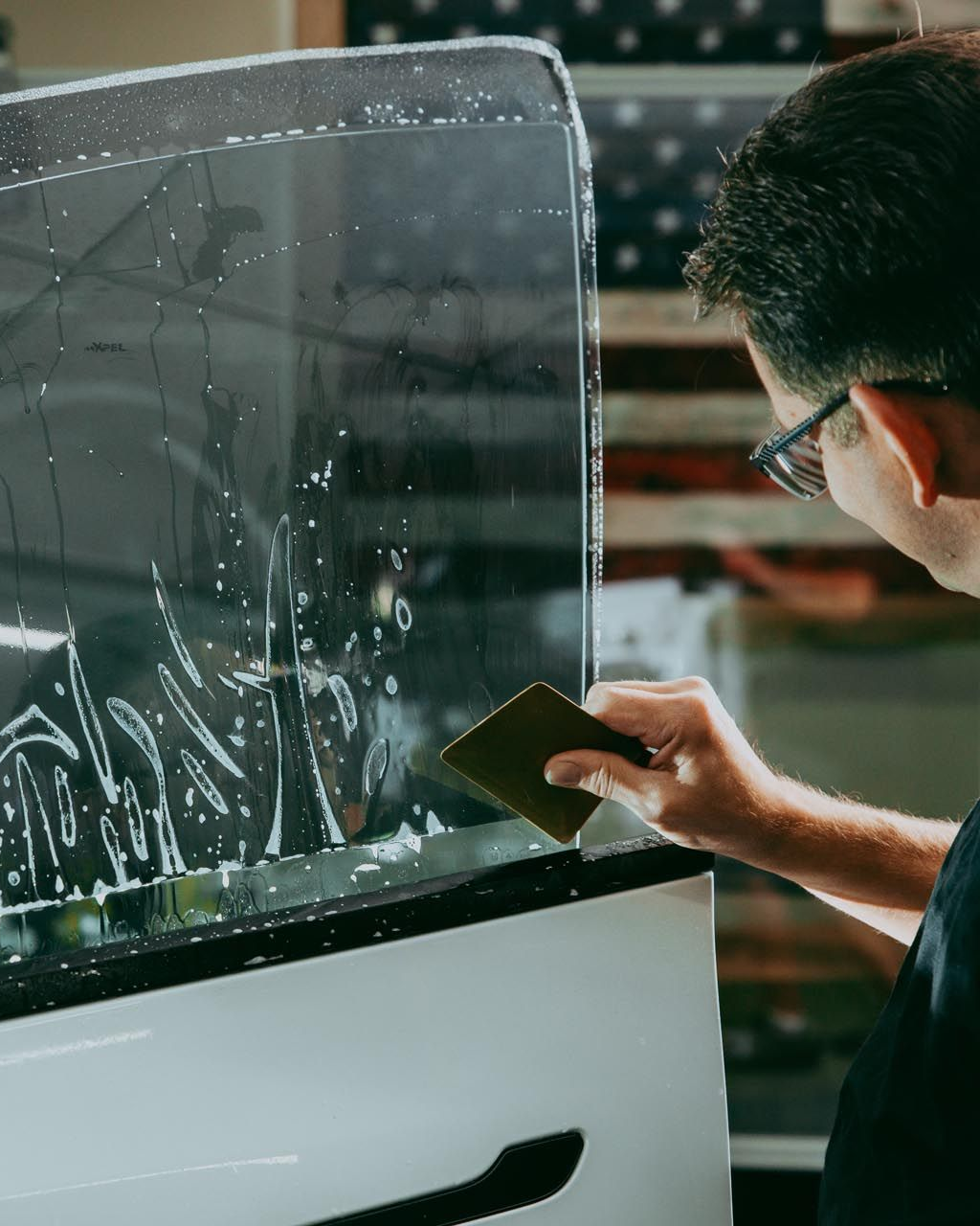 Person scrapes frost from a car window with a card, cleaning the side glass.