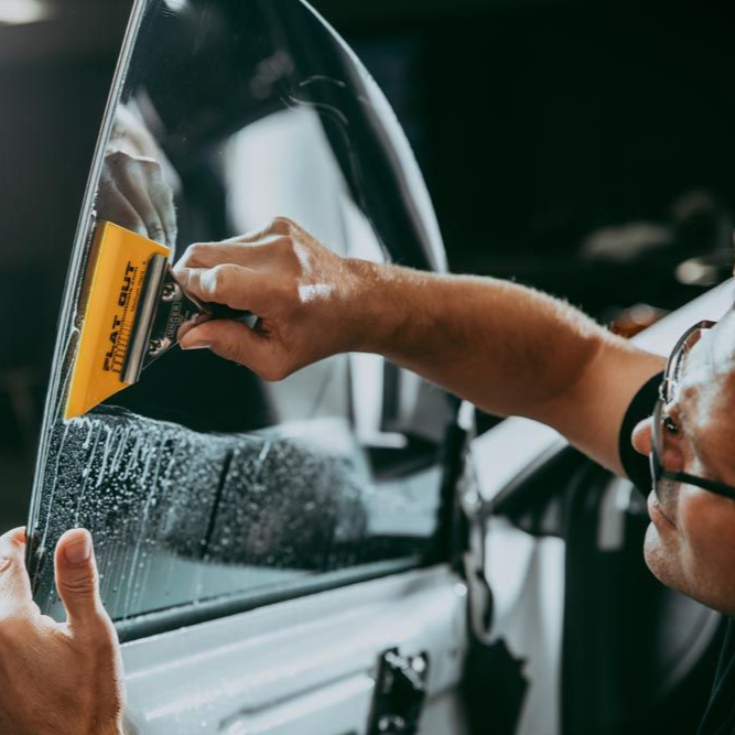 Person scraping frost from a car window with a yellow scraper outdoors