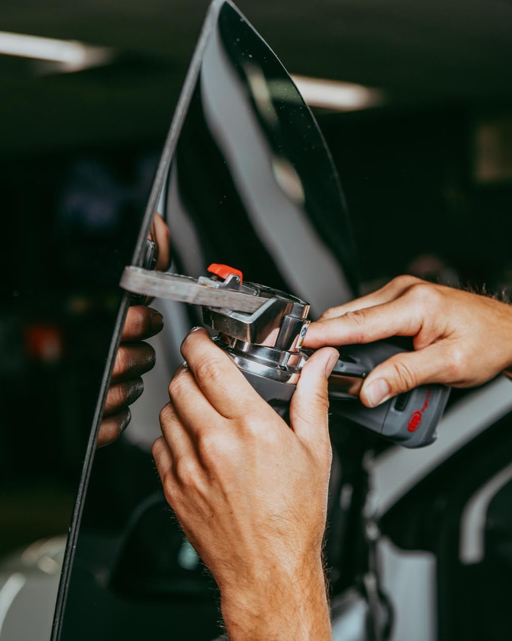 Hands using a tool to trim a clear sheet or panel in a workshop