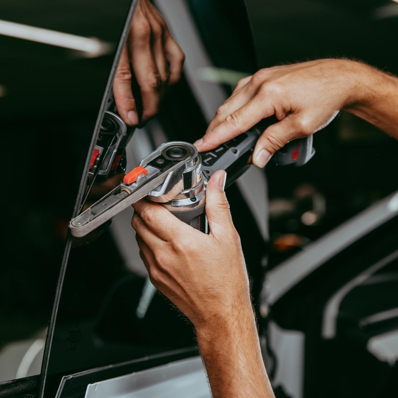 Hands repairing a car side mirror with a tool, close-up view