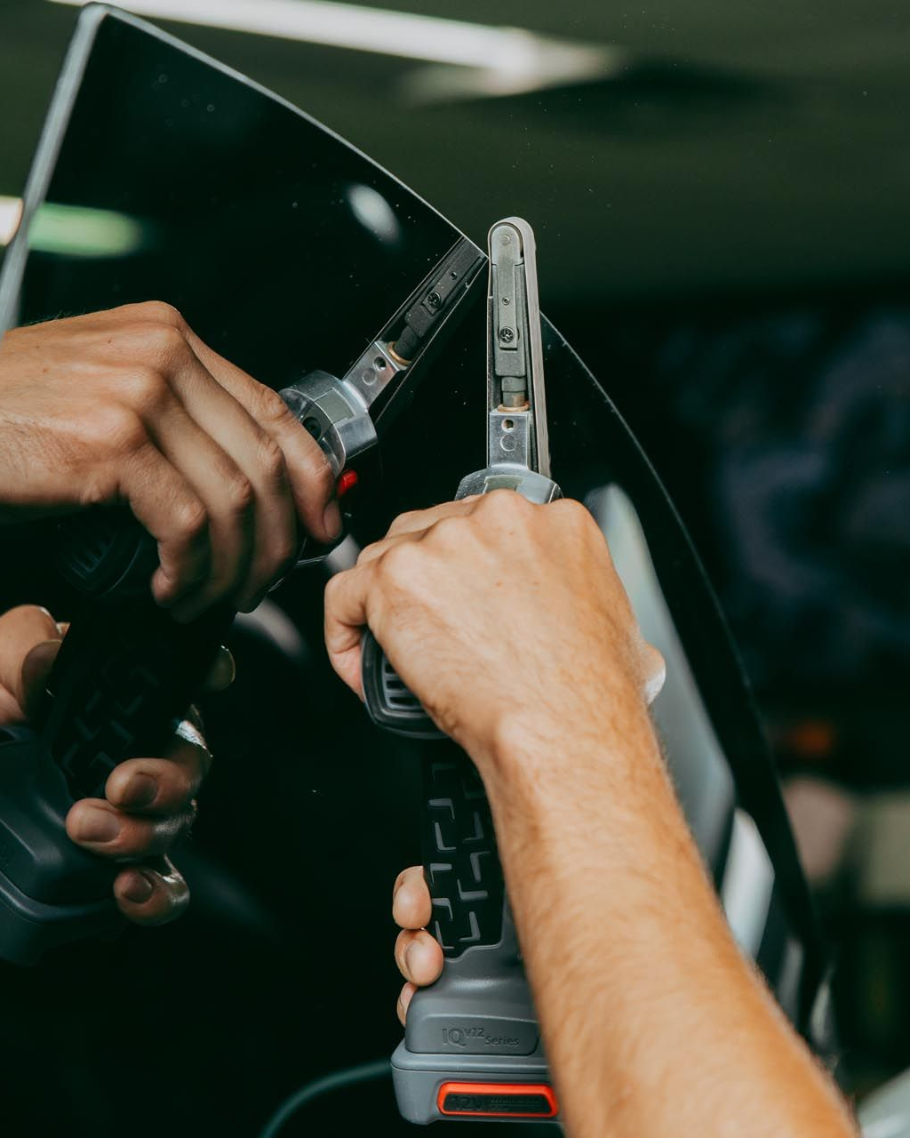 Hands using a drill to fasten a glass pane in a dark workshop