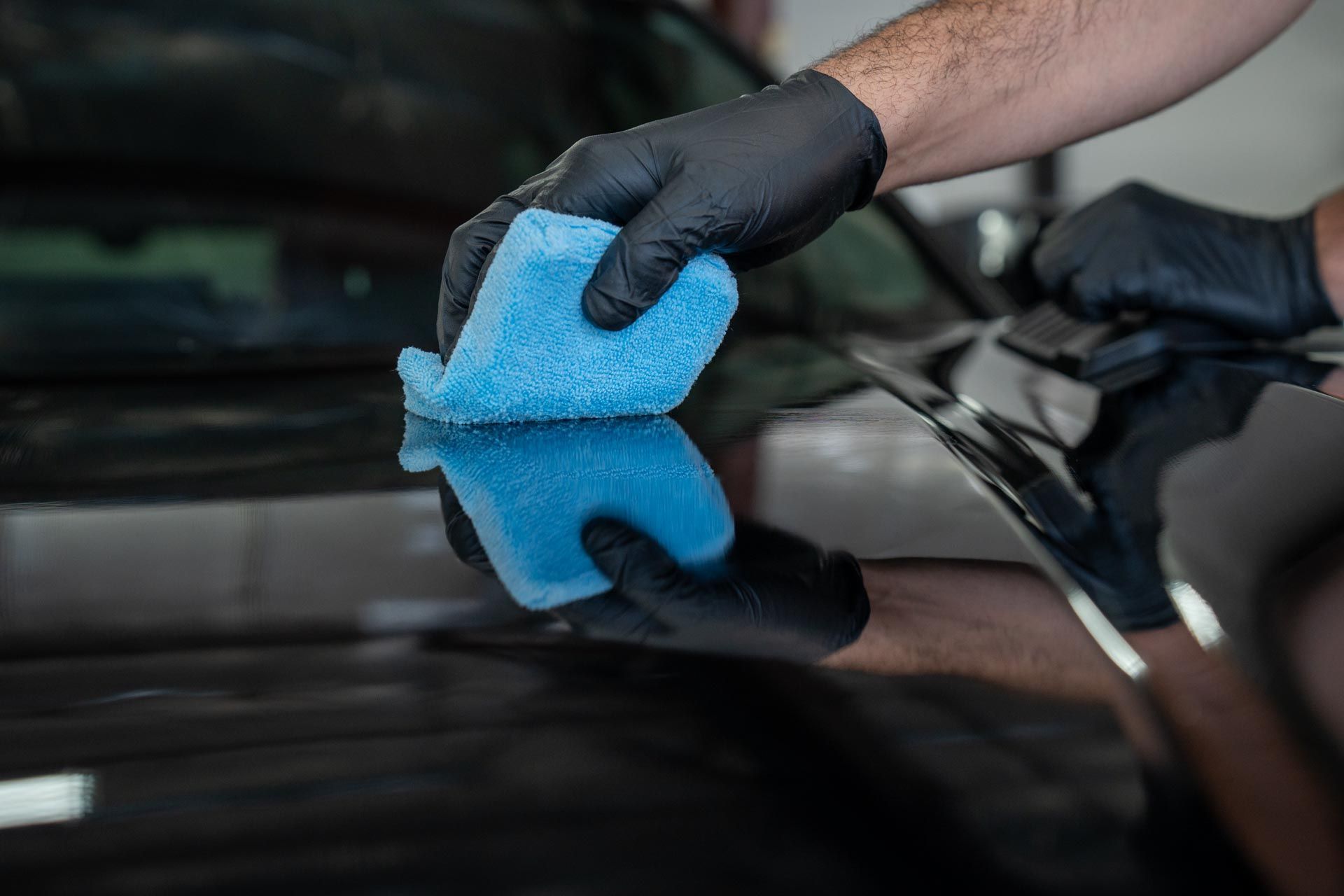Gloved hand wiping a black car window with a blue microfiber cloth
