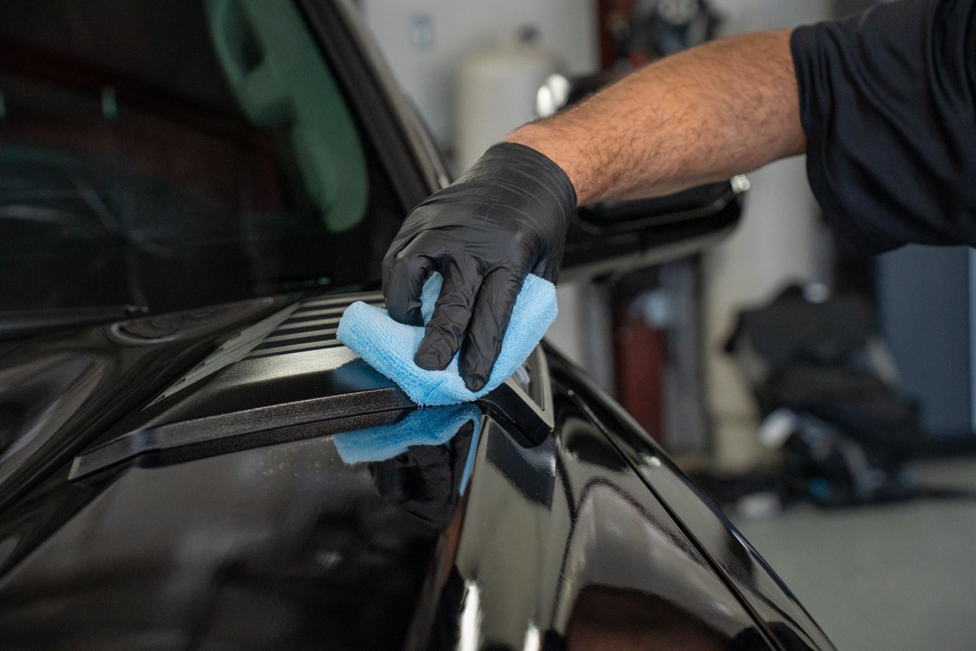 Mechanic polishing a gray car with a buffer in a workshop