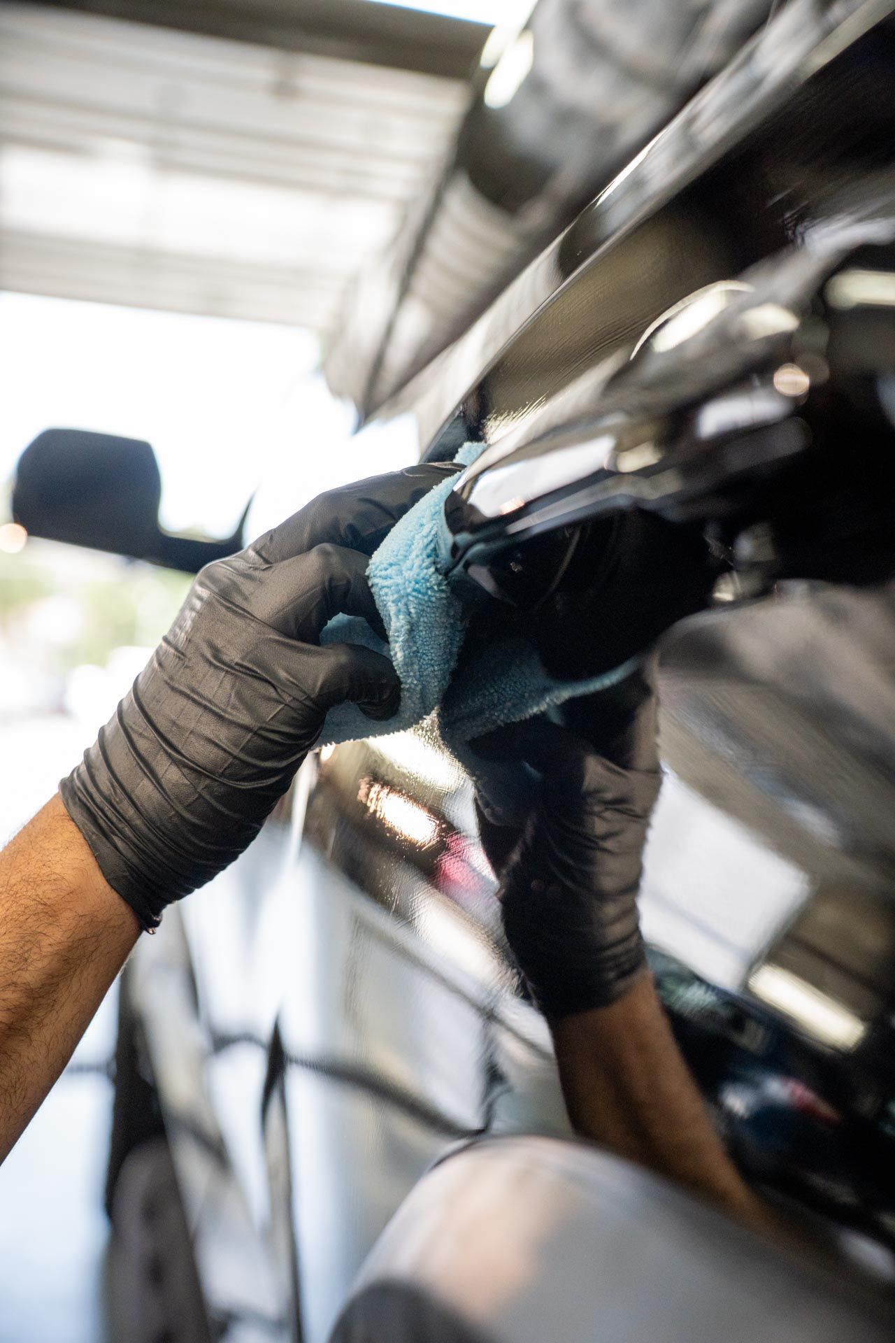 Gloved hands polishing a car’s reflective surface in a garage with a blue cloth