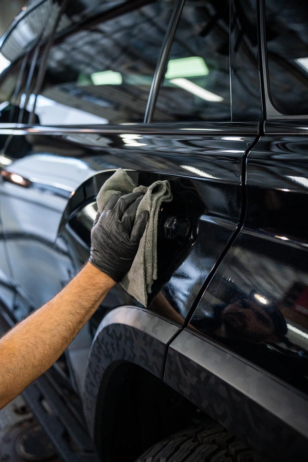 Gloved hand polishing a black car door with a cloth in a garage