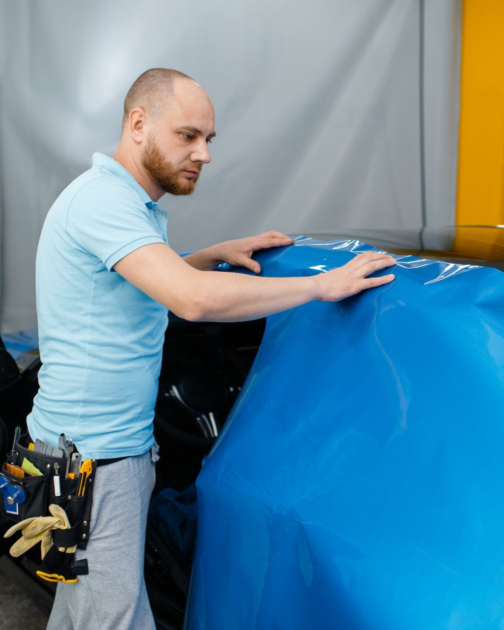 Worker in a light blue shirt adjusting a large blue cover over equipment in a workshop.
