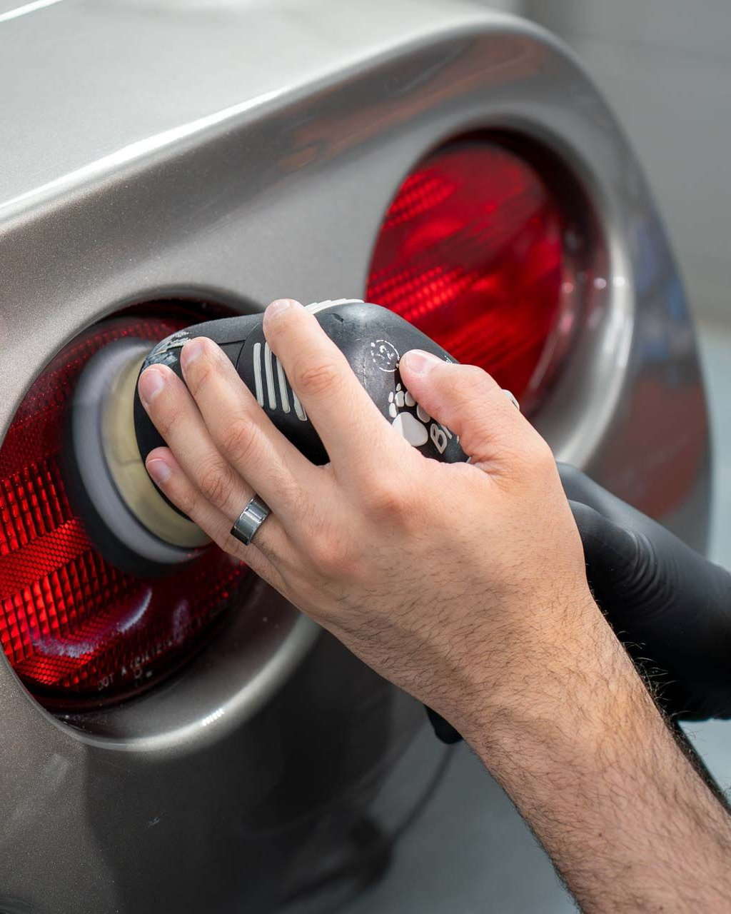 Hand polishing a silver car’s rear light with a cloth, red taillights visible.