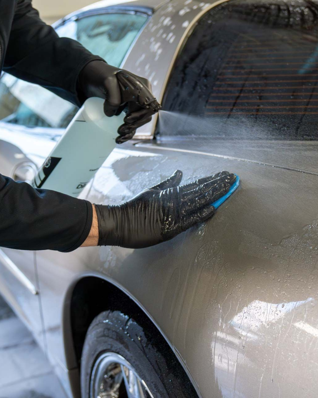 Gloved hands smoothing black film on a silver car window during auto detailing