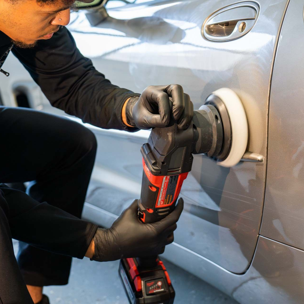 Person using a buffer to polish a silver car door