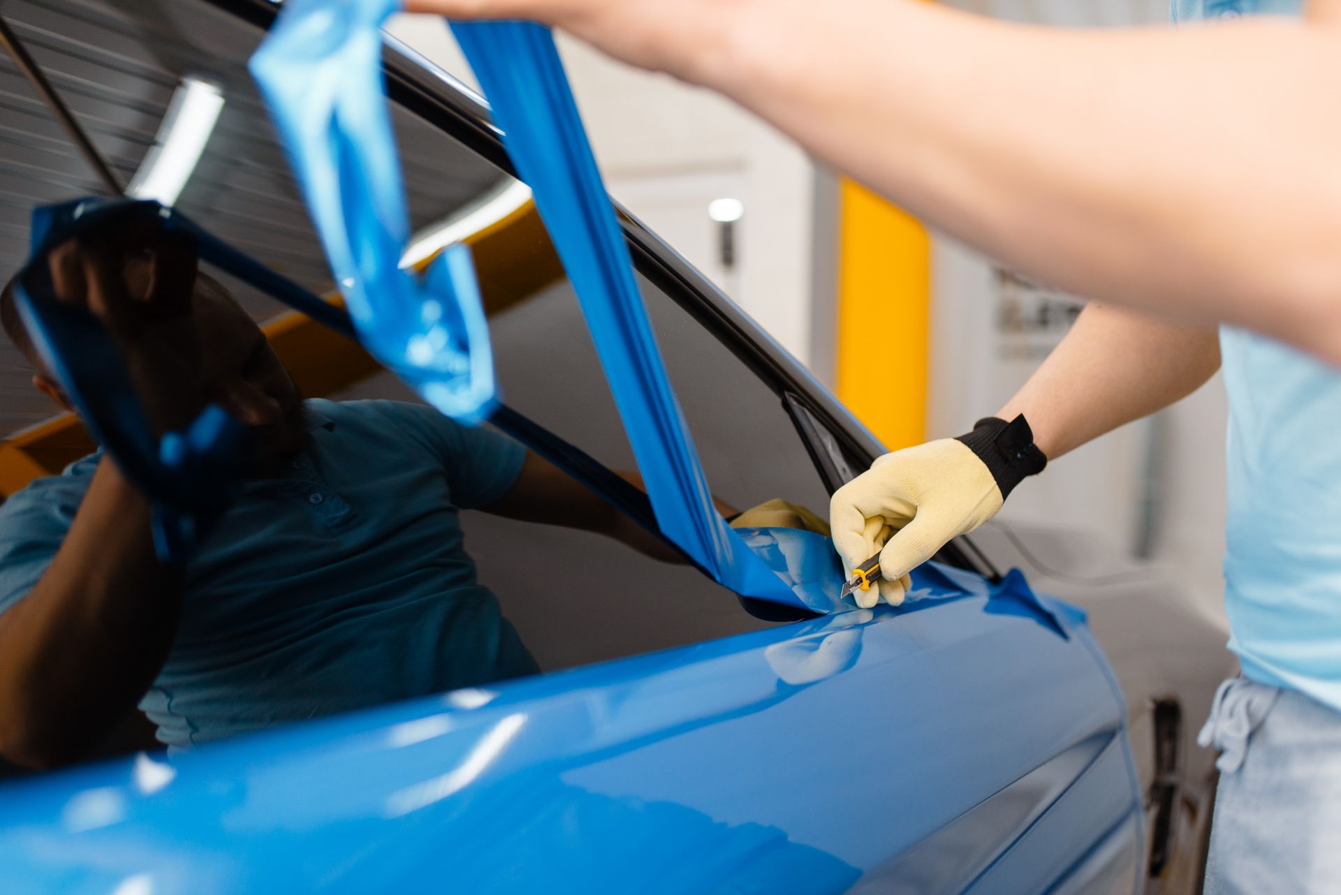 Worker applying blue protective film to a blue car door in a garage